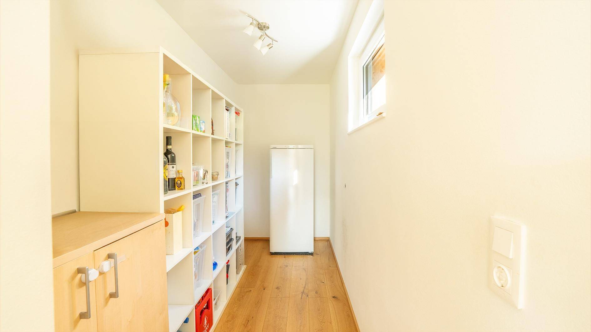 Heller Hauswirtschaftsraum mit Regalen, Kühlschrank und Fenster für natürliche Belichtung.