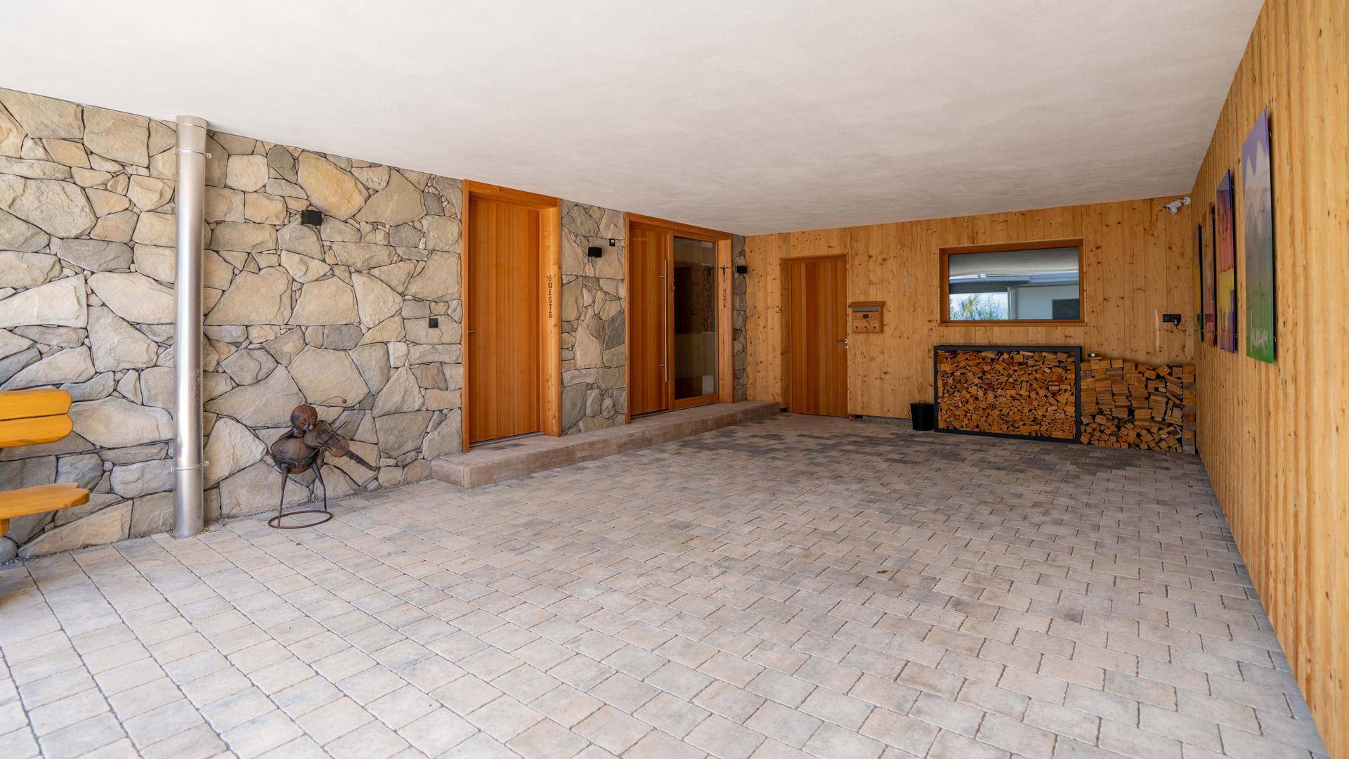 Überdachter Außenbereich mit Steinwand, Holzverkleidung und gepflastertem Boden.