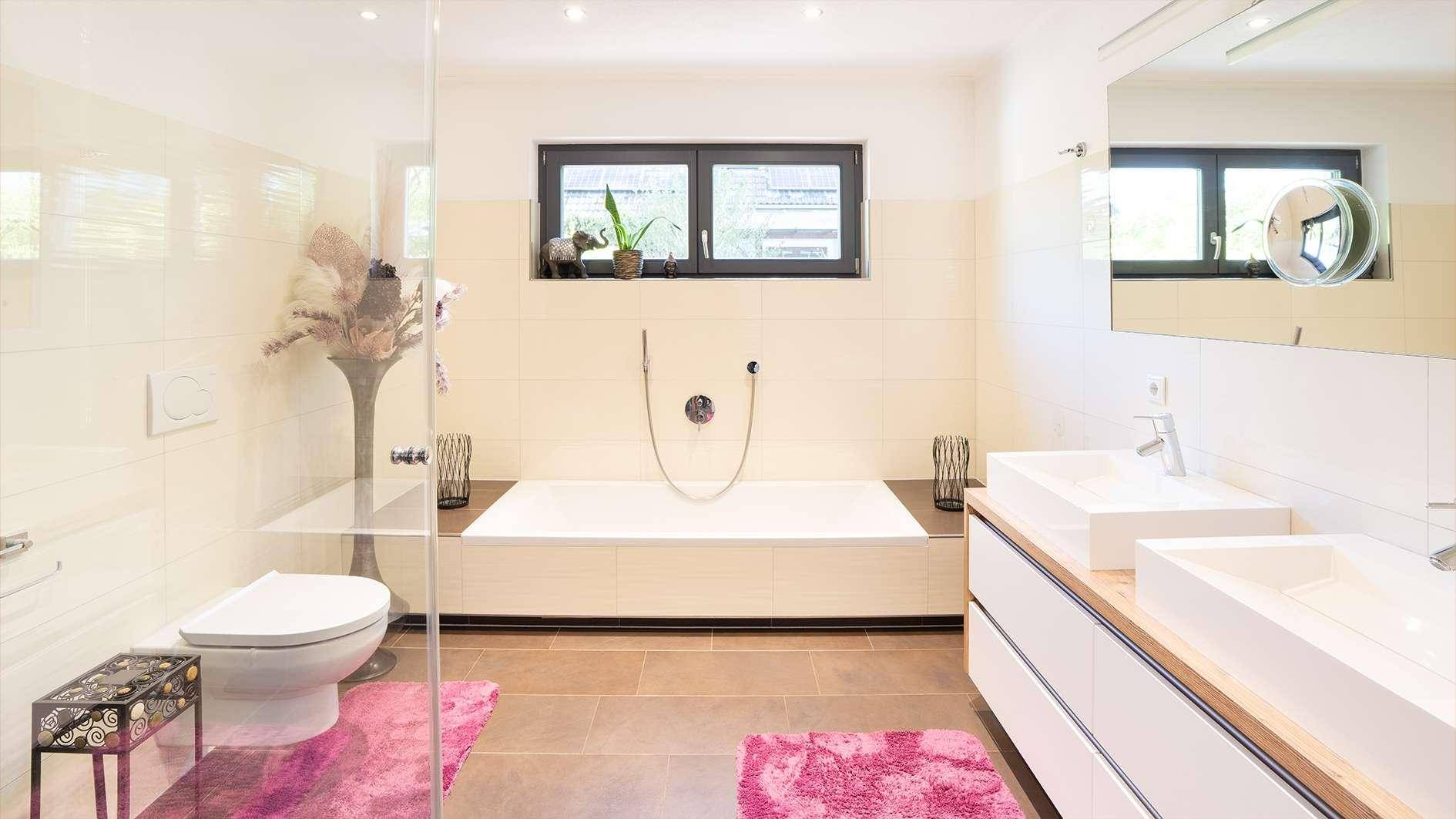 Modernes Badezimmer mit Badewanne, Doppelwaschbecken, Toilette und Fenster für Tageslicht.