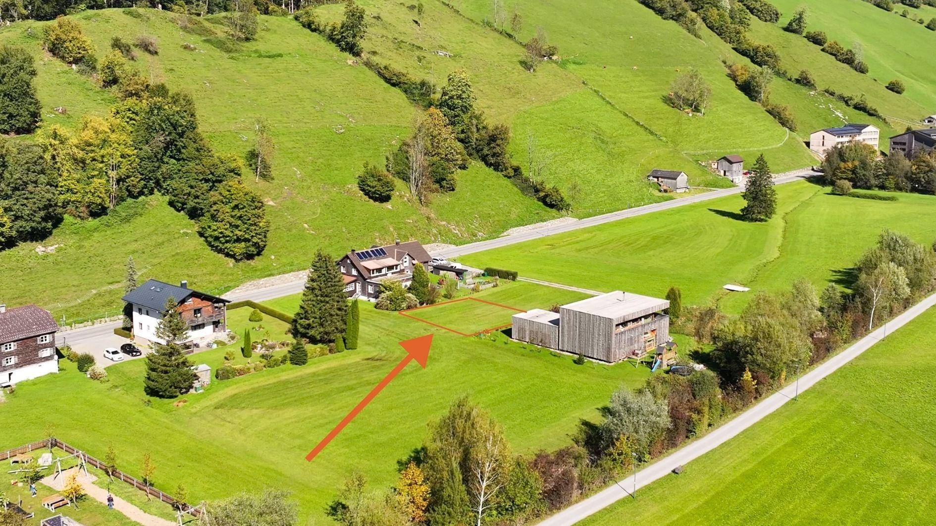 Luftaufnahme des Baugrundstücks, markiert mit einem roten Pfeil, in einer idyllischen ländlichen Umgebung.