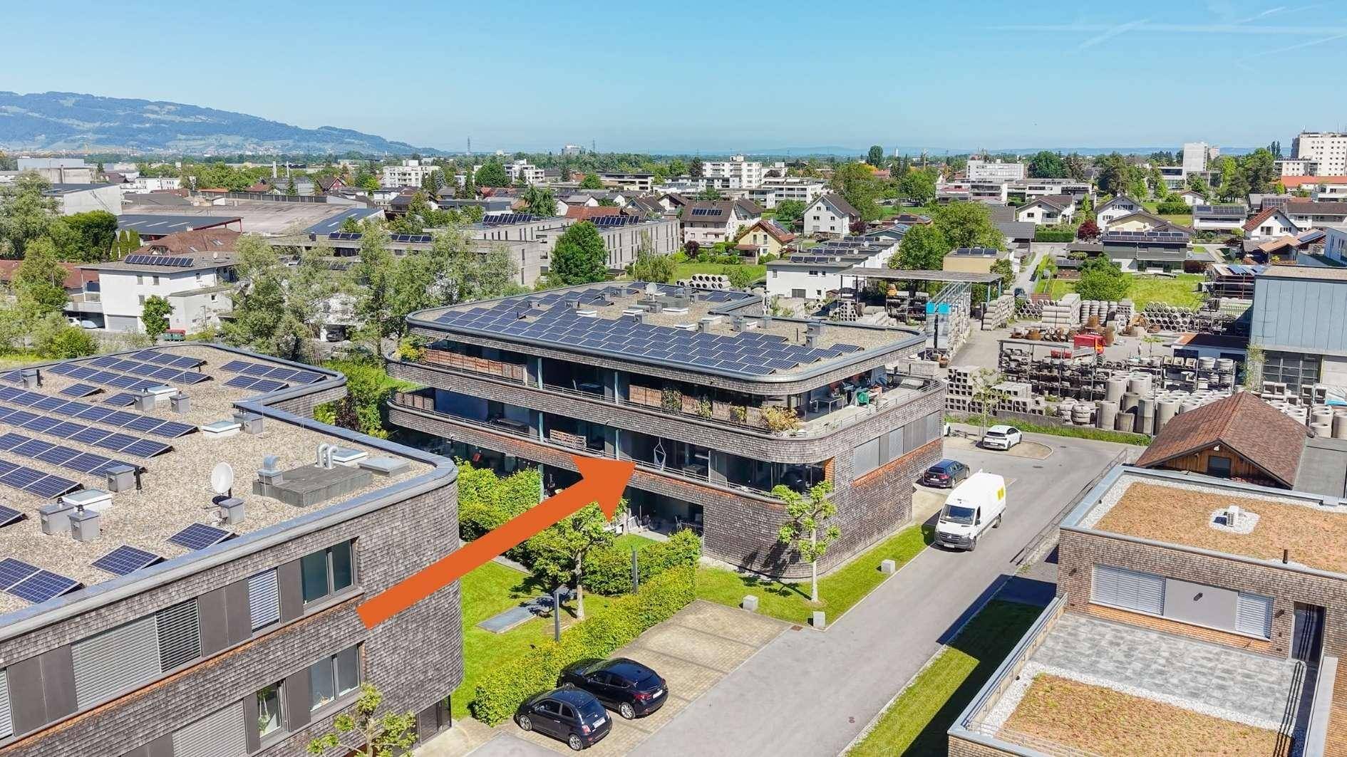Luftaufnahme eines modernen Wohnkomplexes mit Solaranlagen auf dem Dach und städtischer Umgebung.
