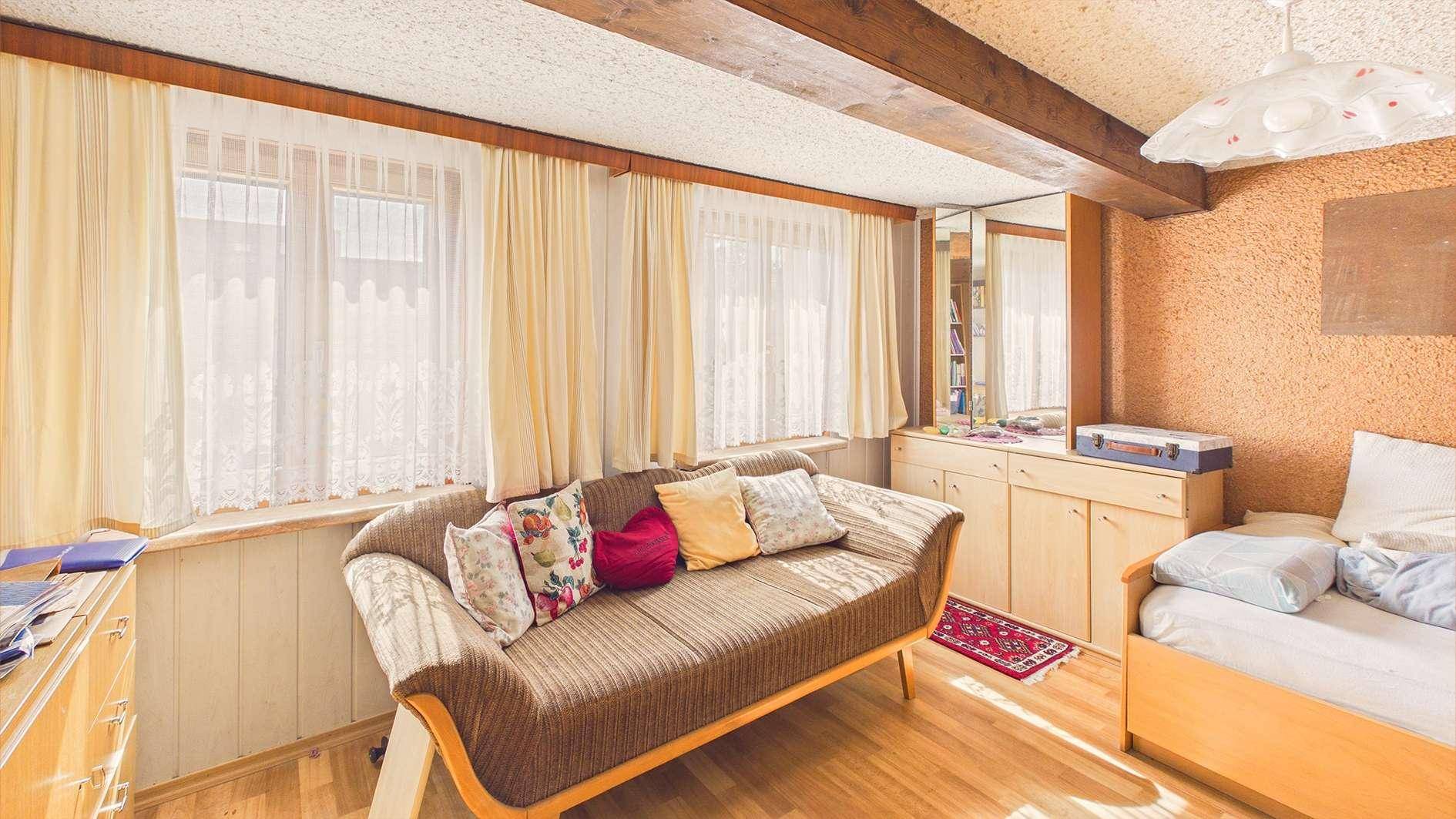 Schlafzimmer mit Tagesbett, Holzboden und großen Fenstern mit Vorhängen.