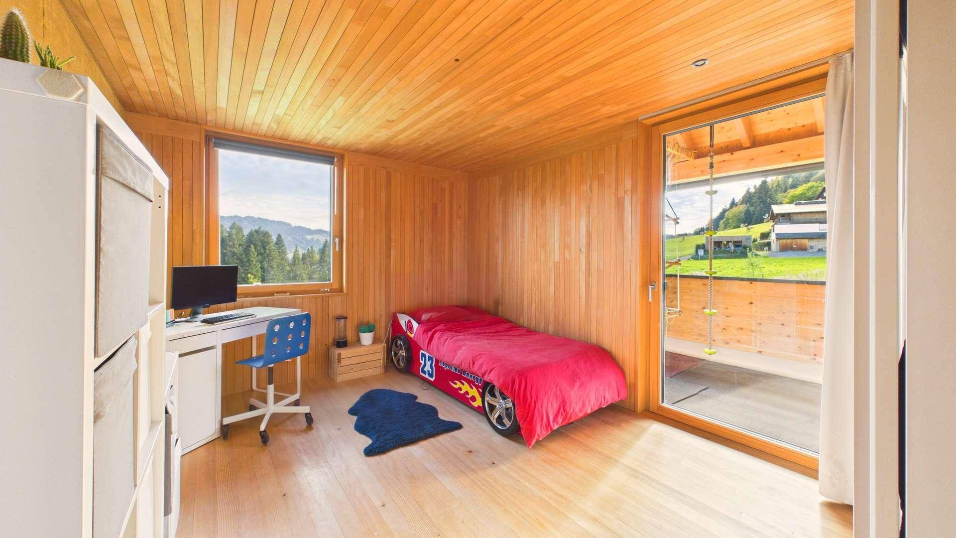 Kinderzimmer mit Holzwänden, Holzboden und Zugang zu einem kleinen Balkon mit Aussicht.