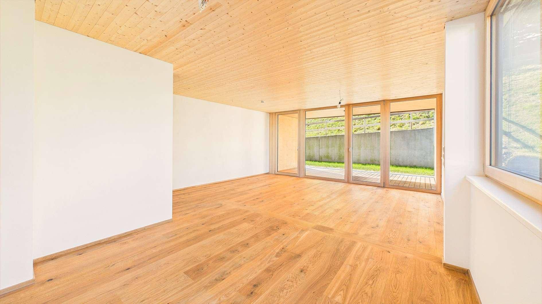 Unmöblierter Raum mit Holzboden, Holzdecke und großen Glasfronten zum Außenbereich.