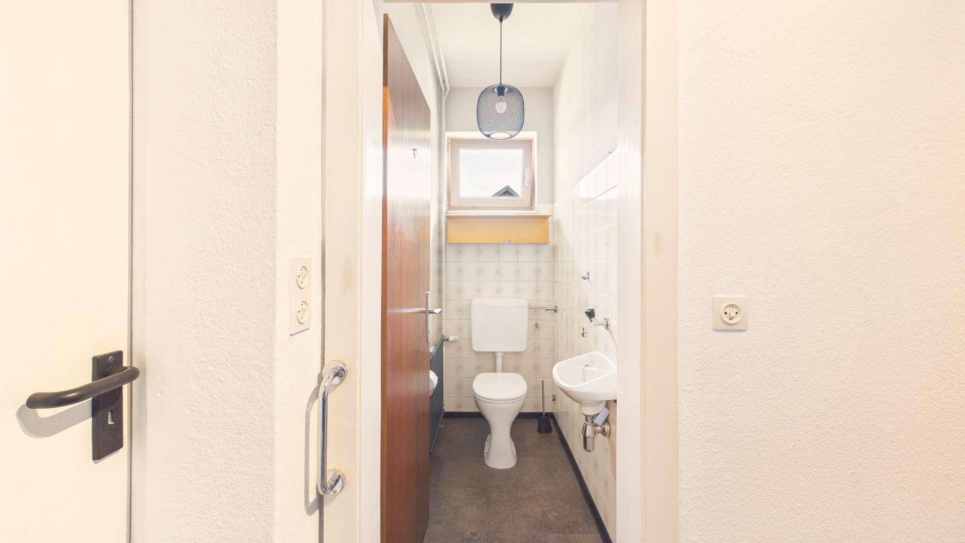 Kleines Gäste-WC mit Fenster, Toilette und Waschbecken, einfach ausgestattet.