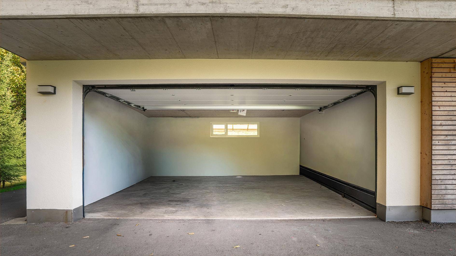 Geräumige Garage mit offenem Tor und kleinem Fenster, bereit zur Nutzung.