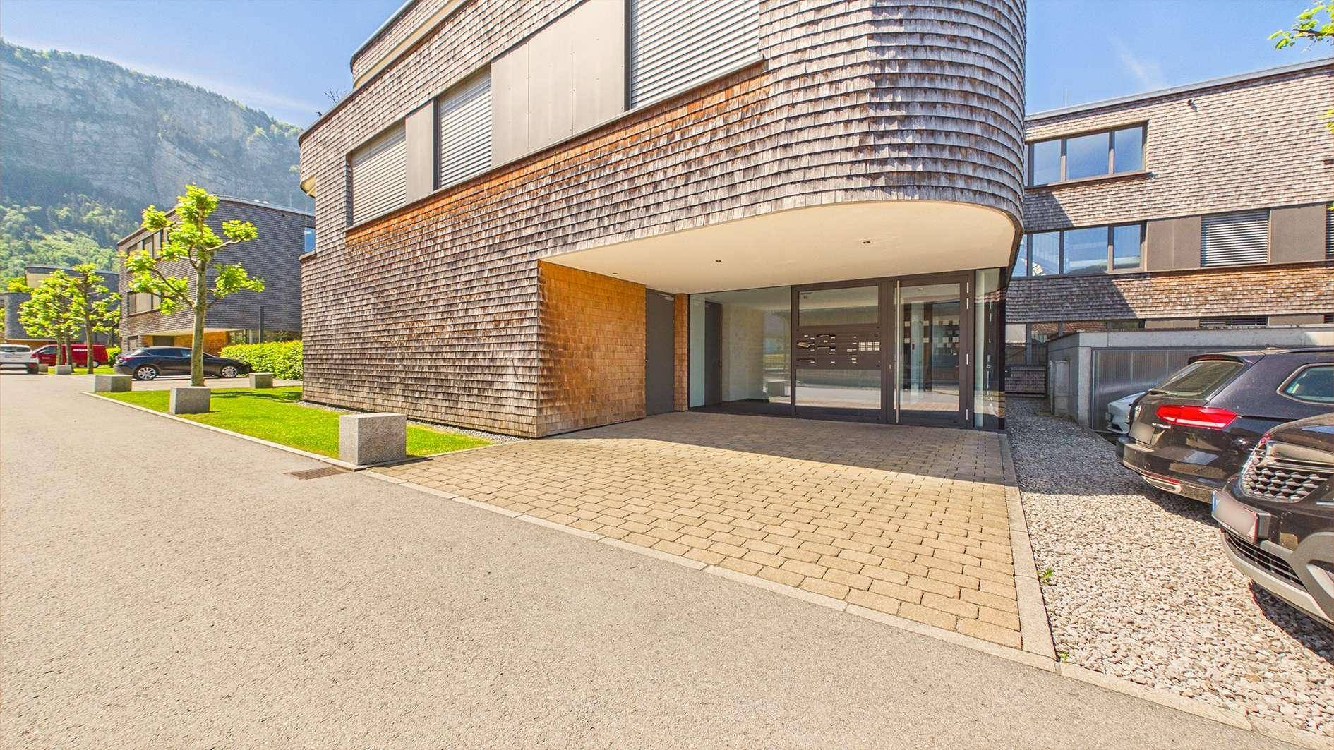 Eingangsbereich eines modernen Gebäudes mit Holzfassade und gepflastertem Zugang.