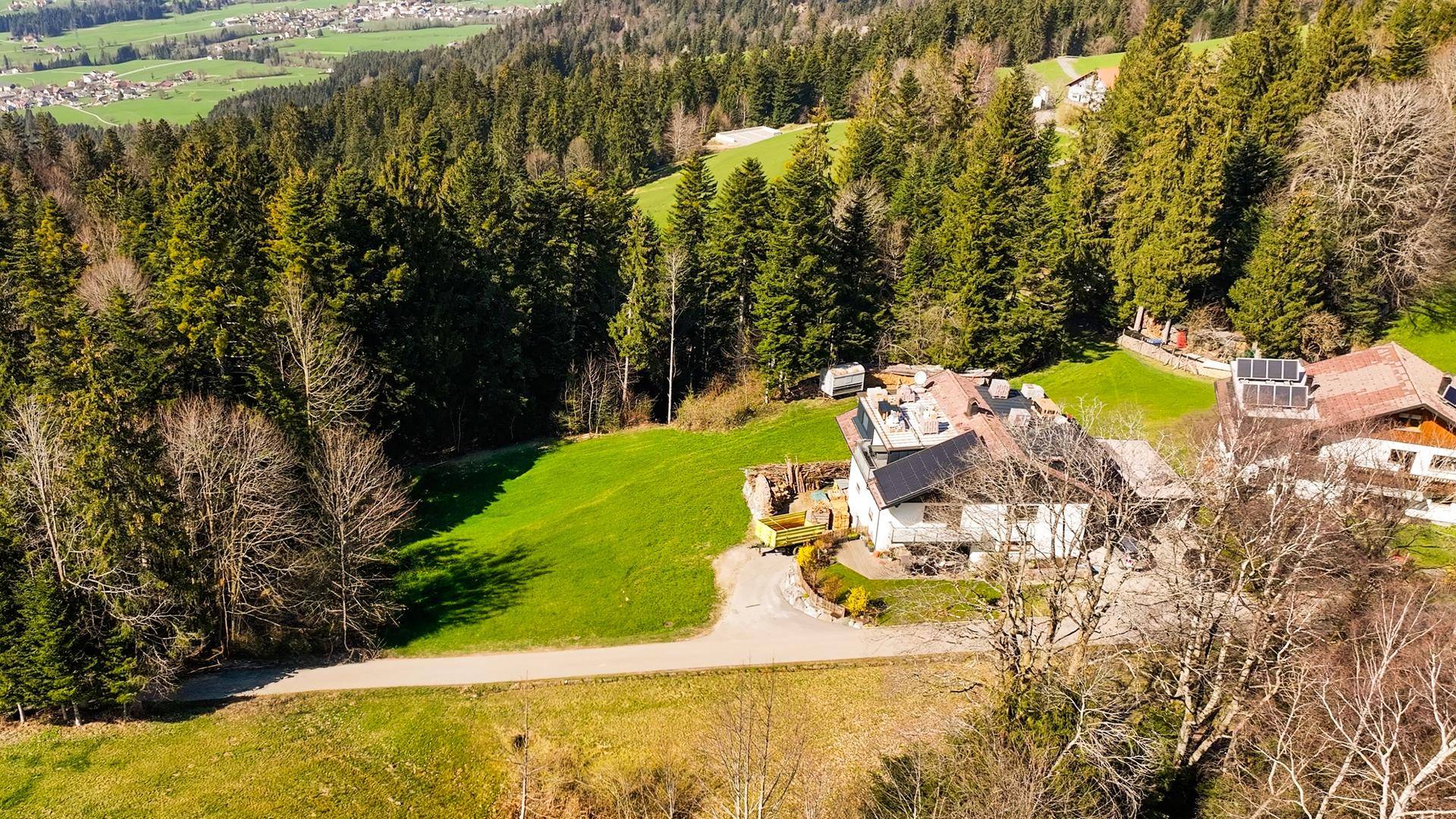 Luftaufnahme eines Hauses umgeben von Wald und grünen Wiesen mit weitem Blick ins Tal.
