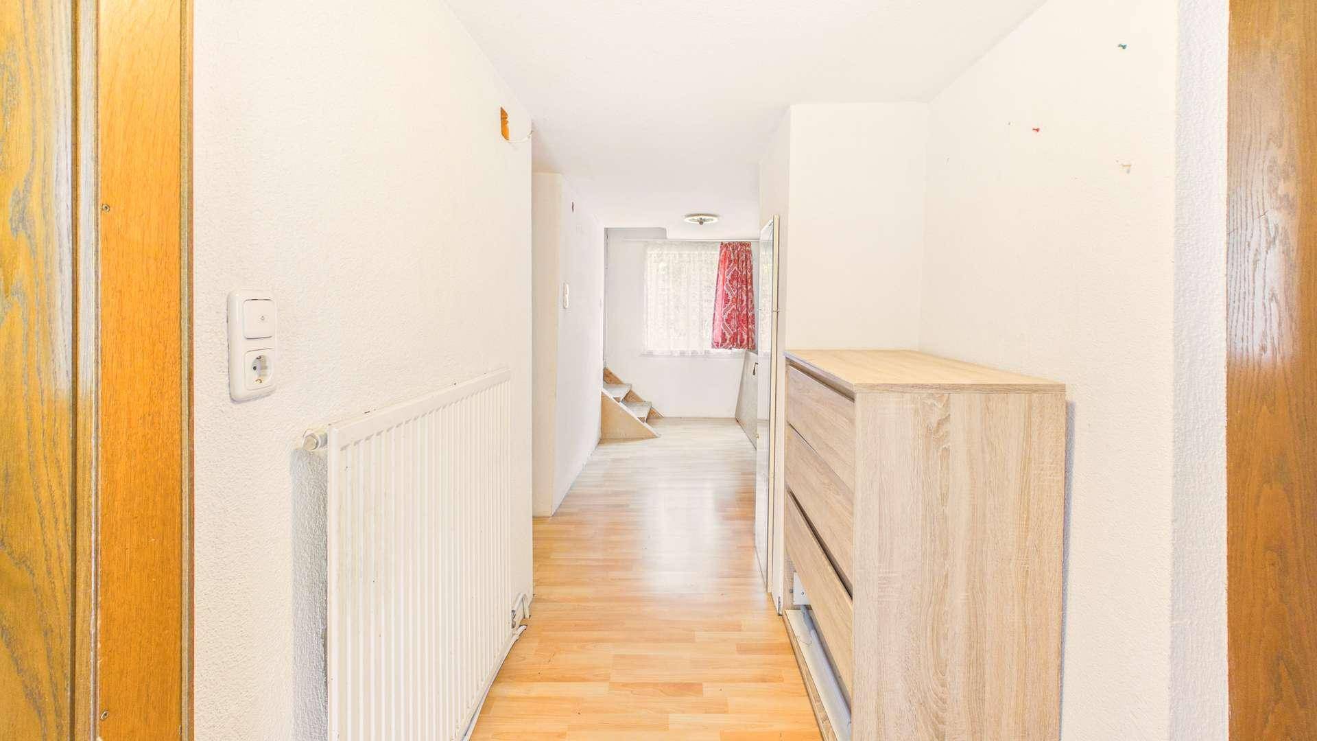 Heller Flur mit Holzboden, weiß gestrichenen Wänden und einer Kommode.