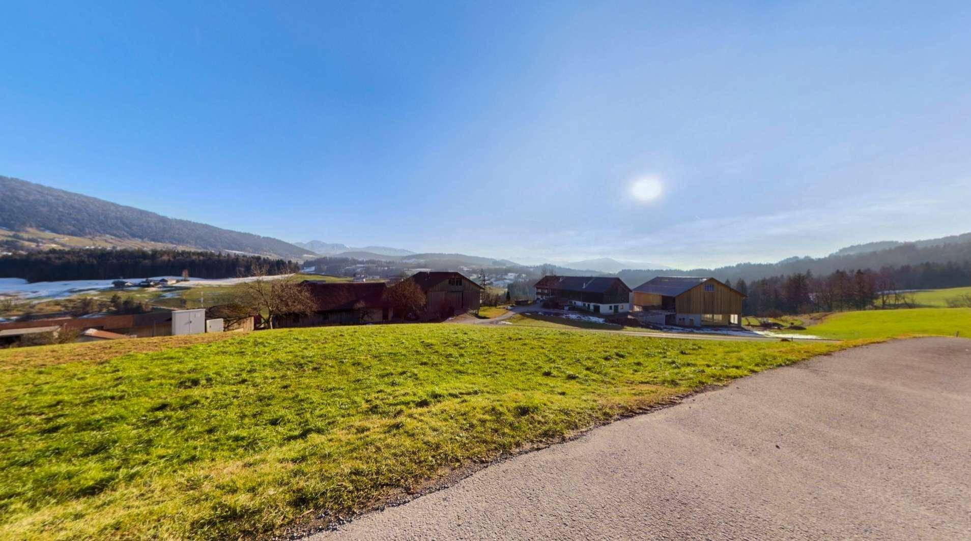 Weitläufige Landschaft mit grünen Wiesen, schneebedeckten Hügeln und Bergblick unter blauem Himmel.