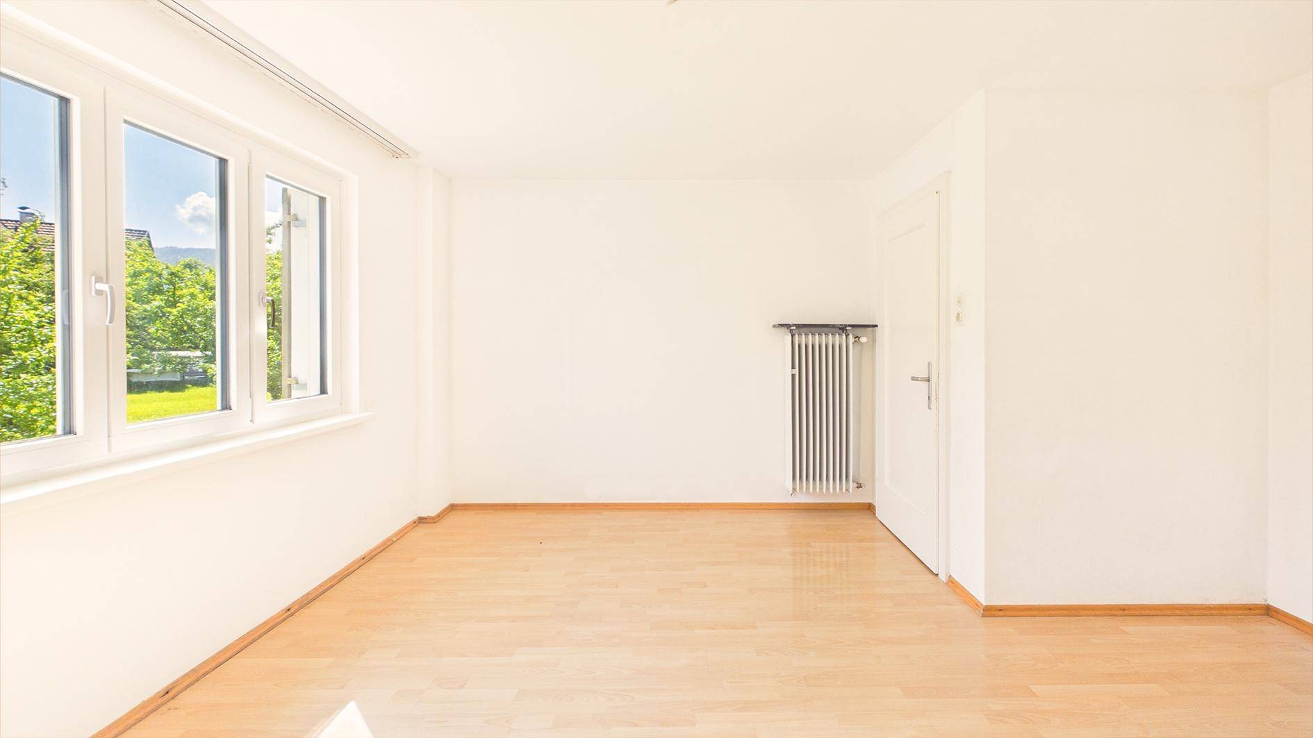 Geräumiges, helles Zimmer mit Holzboden und Fenster, bietet vielseitige Nutzungsmöglichkeiten.
