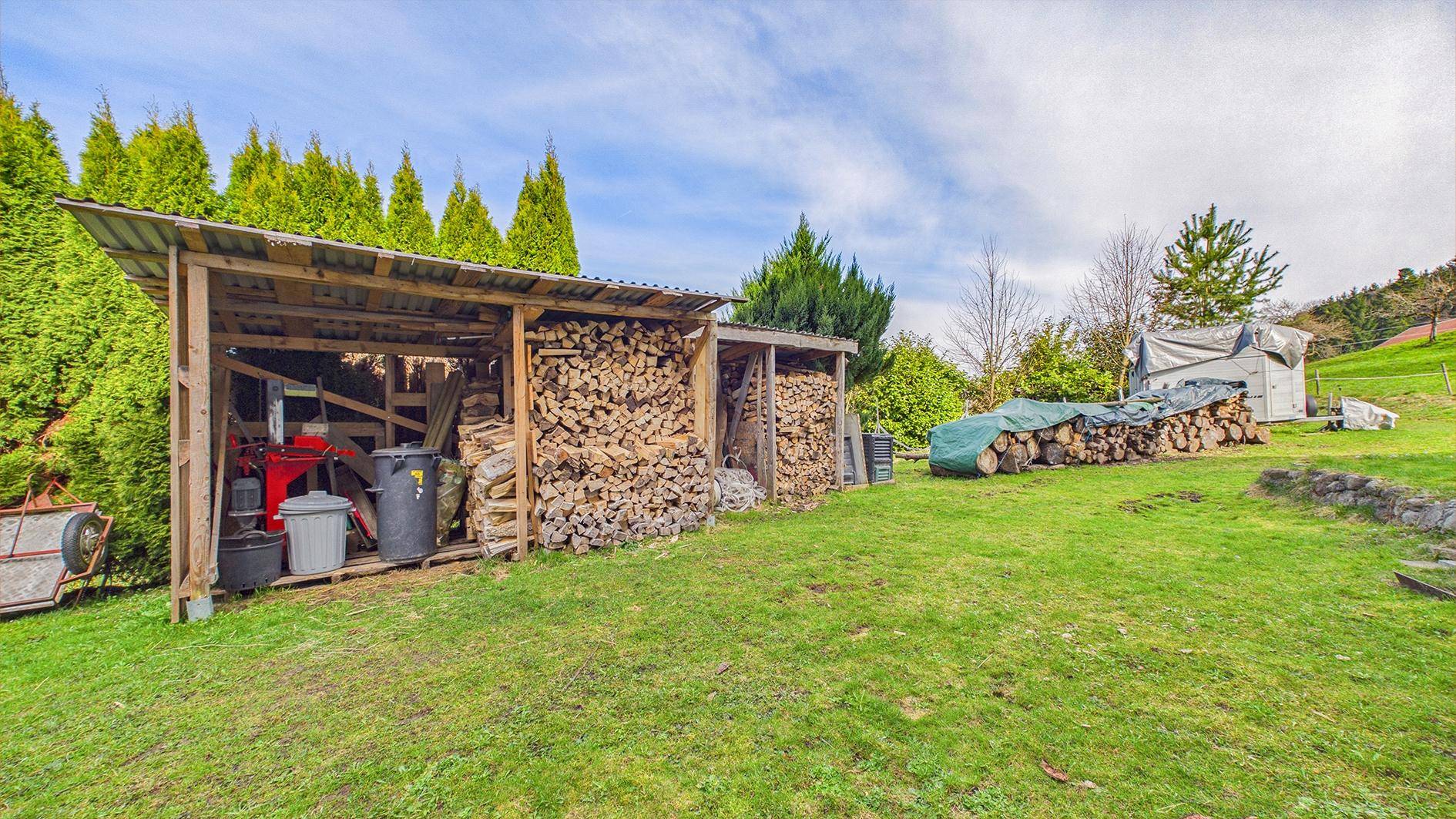 Großer Gartenbereich mit Holzschuppen, Brennholzstapeln und gepflegtem Rasen.