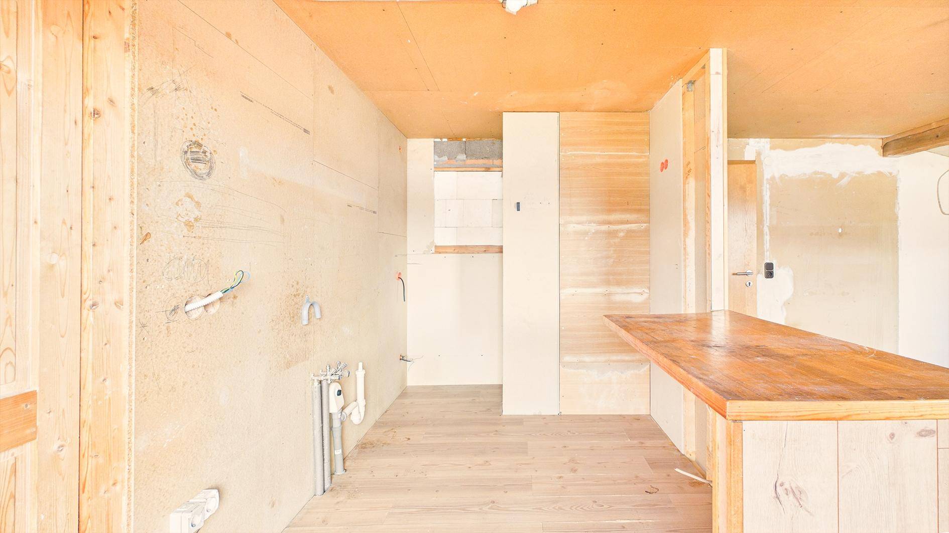 Rohbauküche oder Hauswirtschaftsraum mit sichtbaren Installationen und Holzboden.