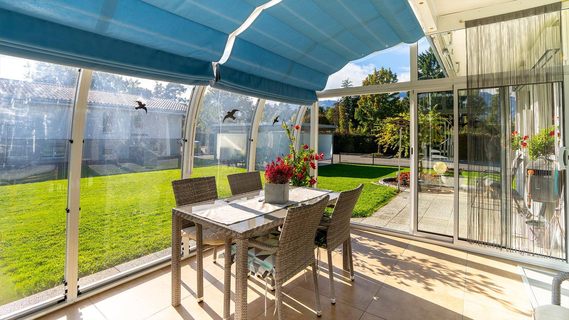 Heller Wintergarten mit Esstisch, Glaswänden und Blick in den Garten.