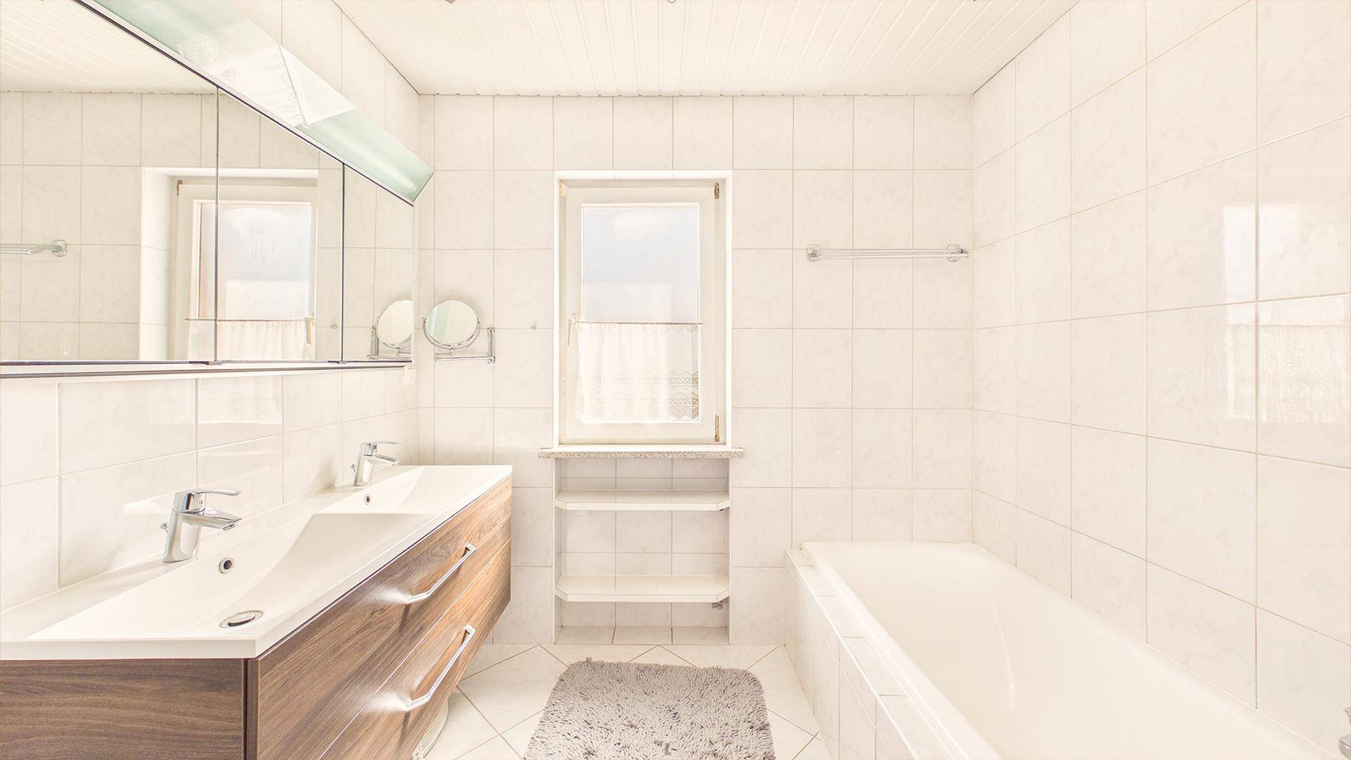 Modernes Badezimmer mit Doppelwaschbecken, Badewanne und großen weißen Fliesen.