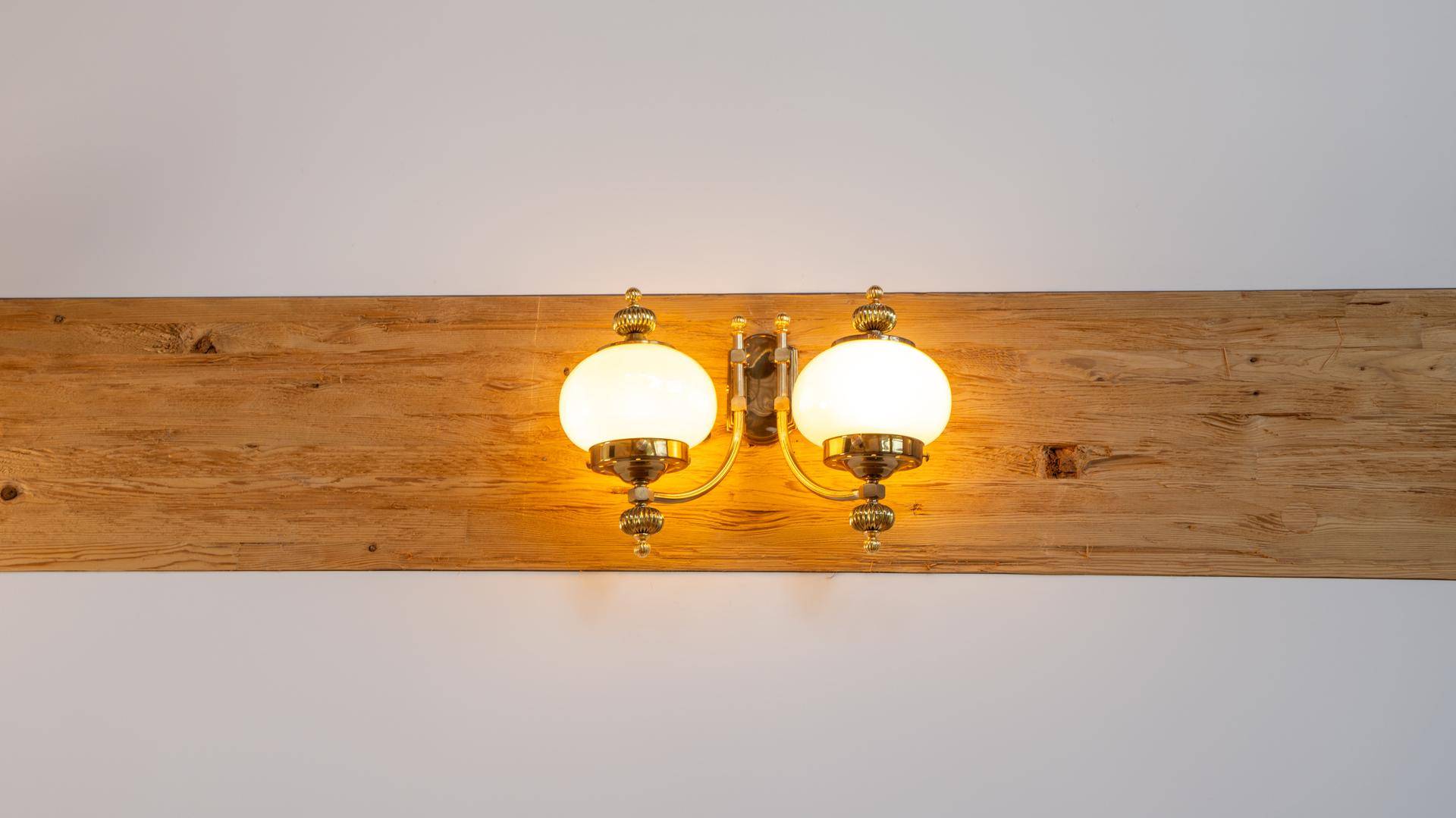 Wandleuchte im klassischen Stil auf einem Holzbalken, die warmes Licht spendet.
