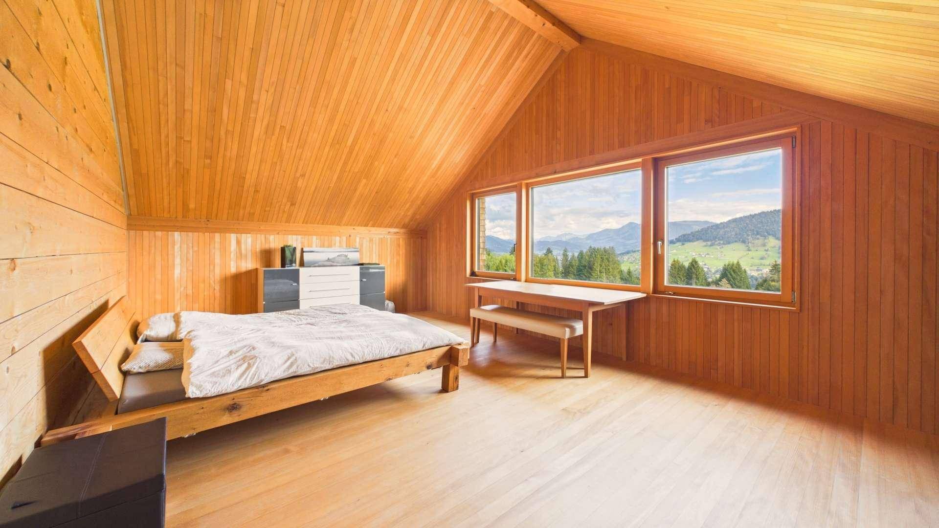 Geräumiges Schlafzimmer im Dachgeschoss mit Holzausstattung und Panoramablick auf die Landschaft.