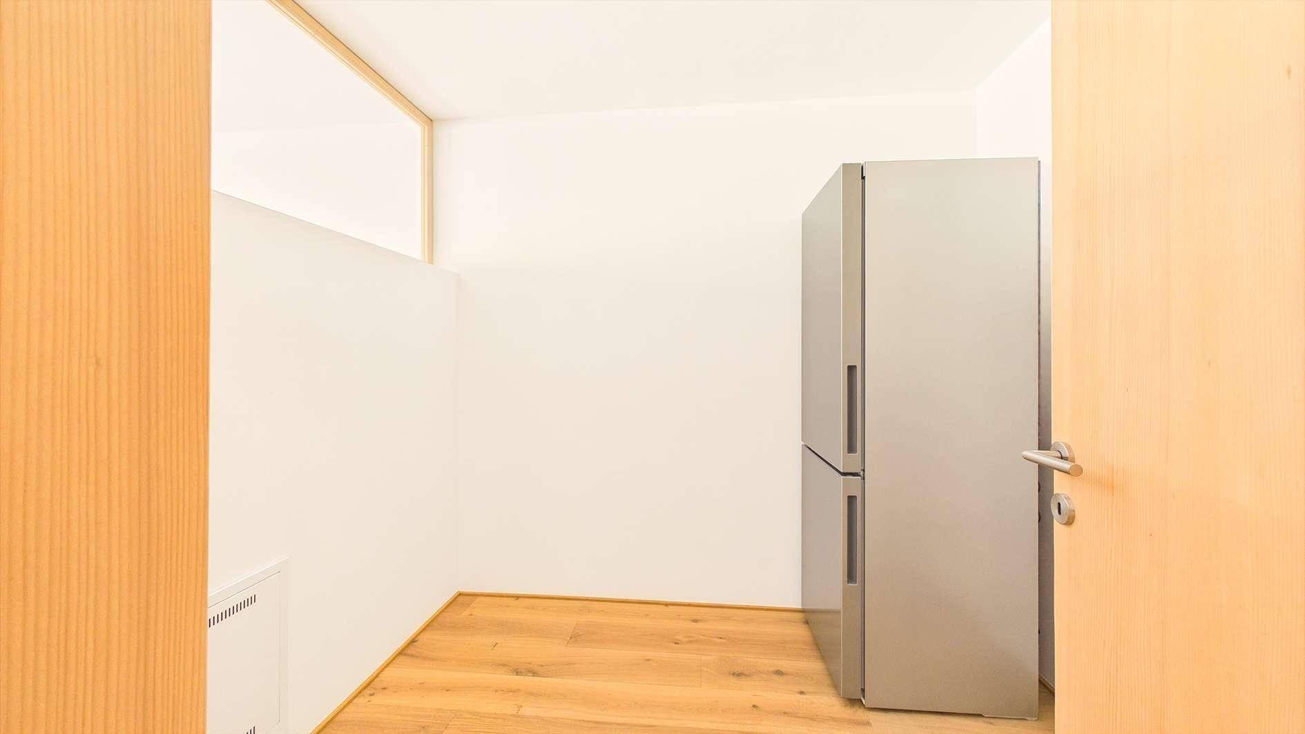 Kleiner Abstellraum oder Speisekammer mit einem großen Kühlschrank und Holzboden.
