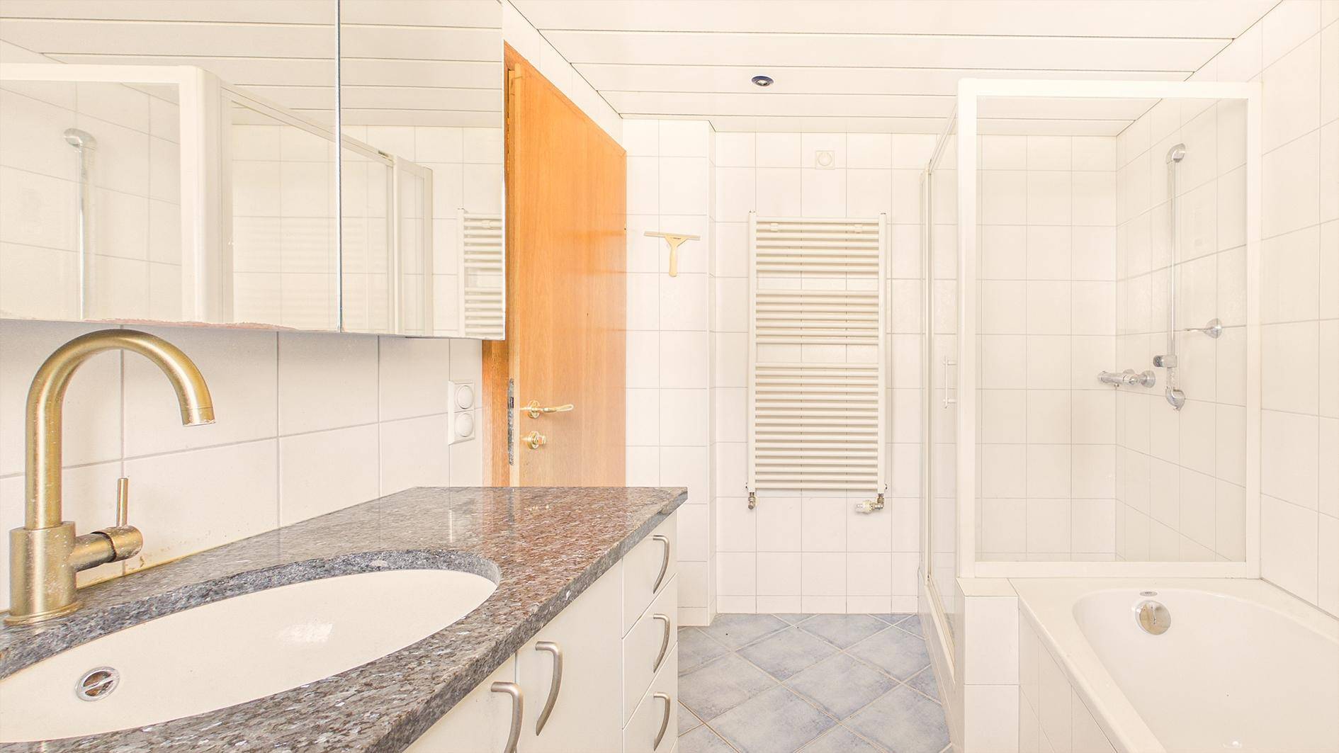 Helles Badezimmer mit weißen Fliesen, Granit-Waschtisch und integrierter Badewanne mit Dusche.