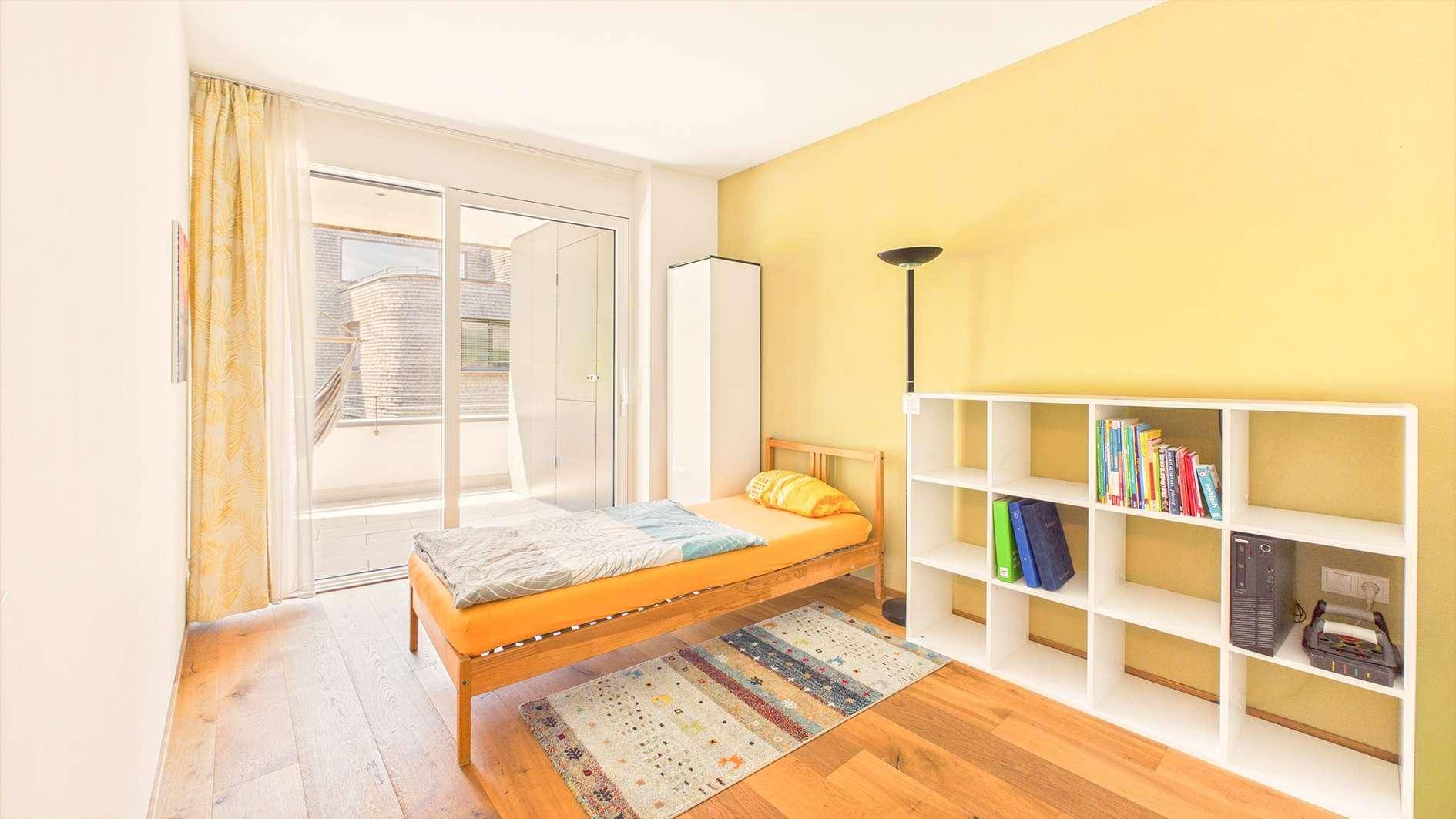 Schlafzimmer mit Holzboden, gelber Wand und Zugang zu einem Balkon.