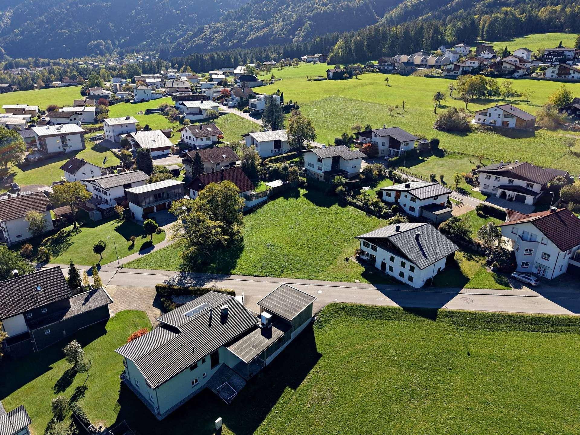 Luftaufnahme einer Wohnsiedlung mit Einfamilienhäusern und grünen Gärten in ländlicher Umgebung.