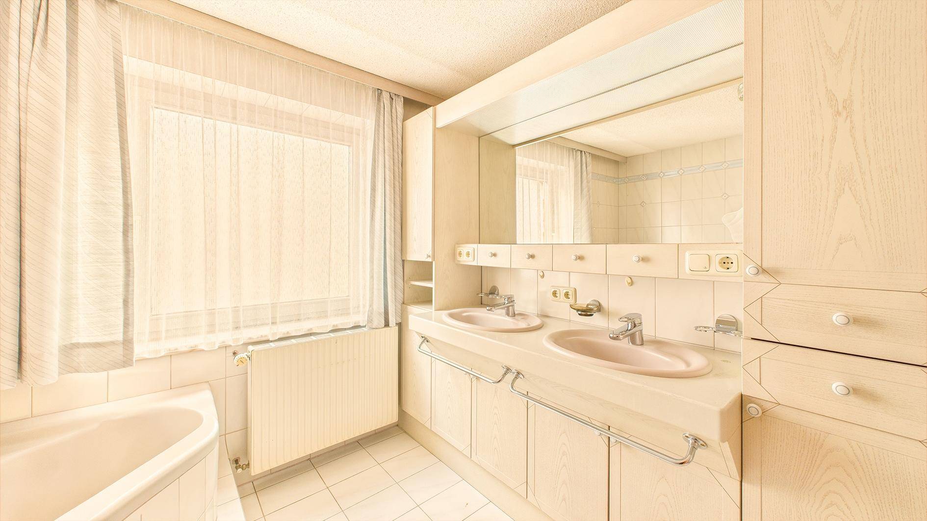 Geräumiges Badezimmer mit Doppelwaschbecken, Badewanne und Fenster, in hellem Design der 80er.