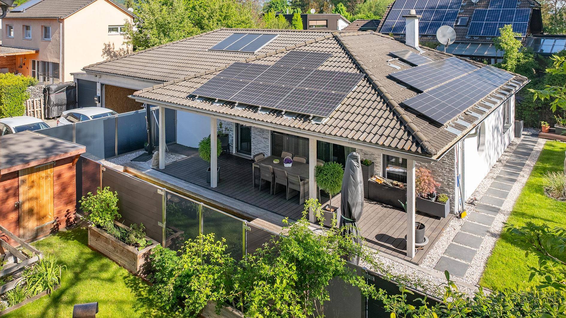 Luftaufnahme des Hauses mit Solaranlagen auf dem Dach und einer großen überdachten Terrasse.