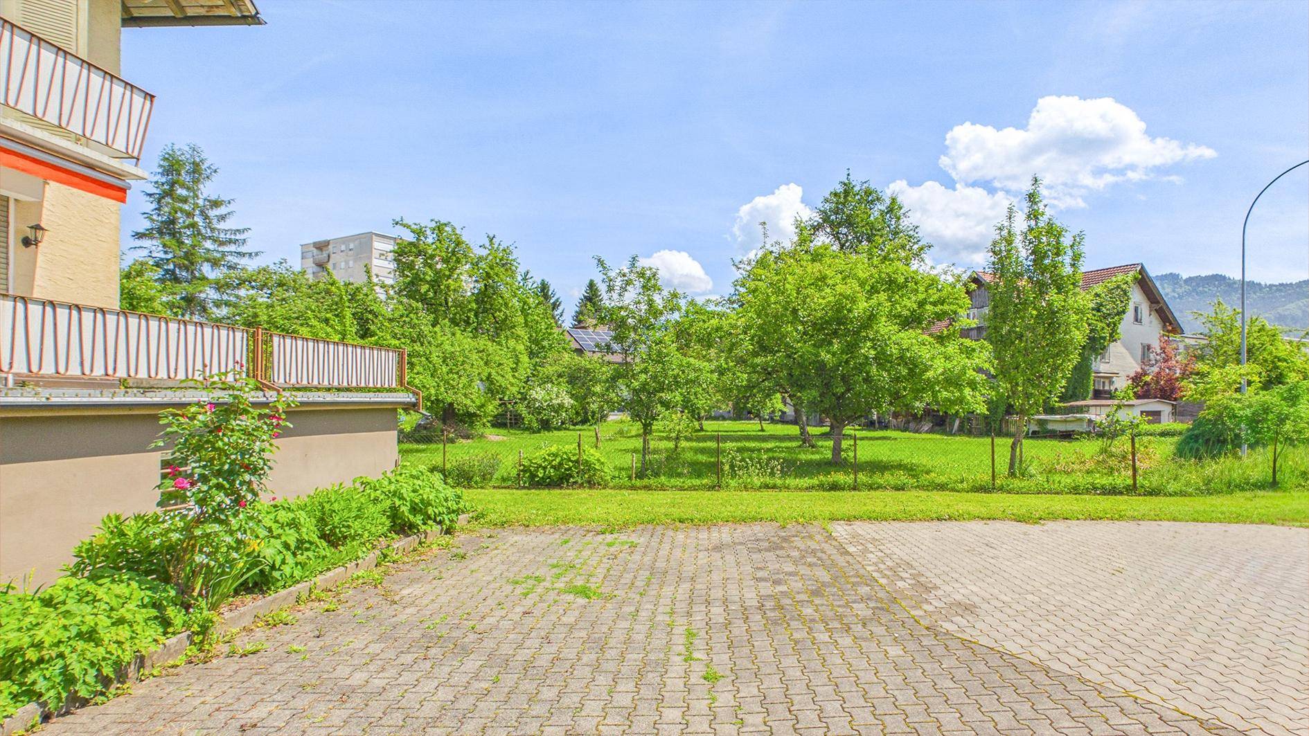 Gepflasterter Parkplatz vor dem Gebäude mit weitem Blick auf den grünen Gartenbereich.