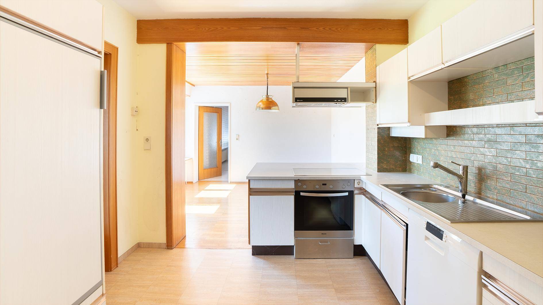 Funktionale Küche mit weißen Schränken, integrierten Geräten und Holzbalken an der Decke.