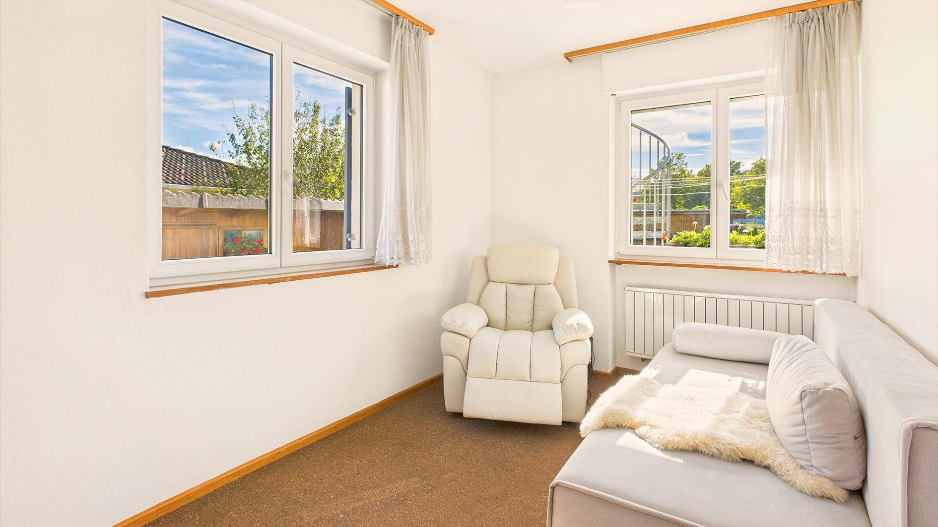 Helles Zimmer mit Teppichboden, Sessel und Sofa, ideal als Büro oder Gästezimmer.