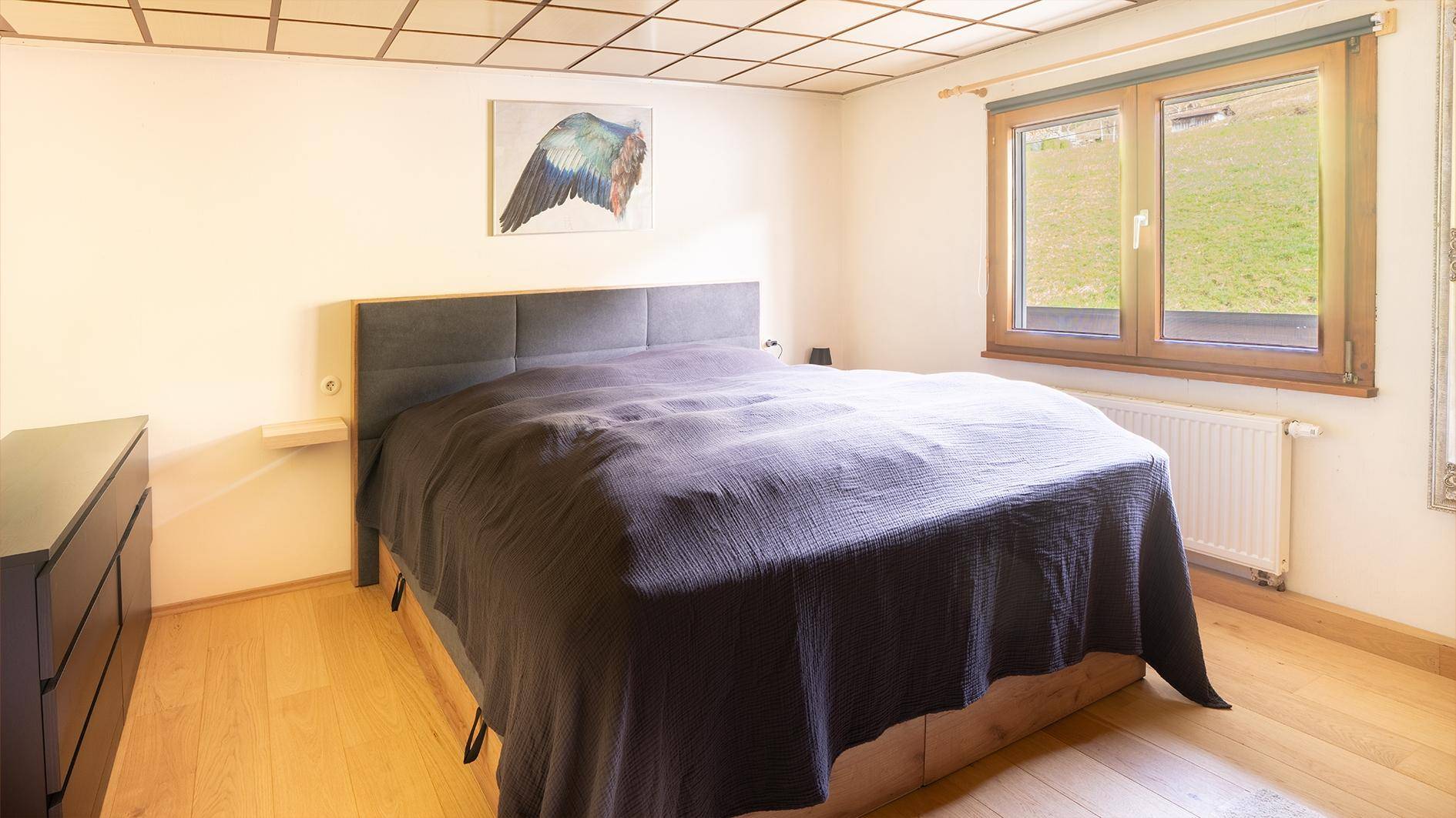 Schlafzimmer mit Holzboden, großem Bett und Fenster mit Blick auf die umliegende Natur.
