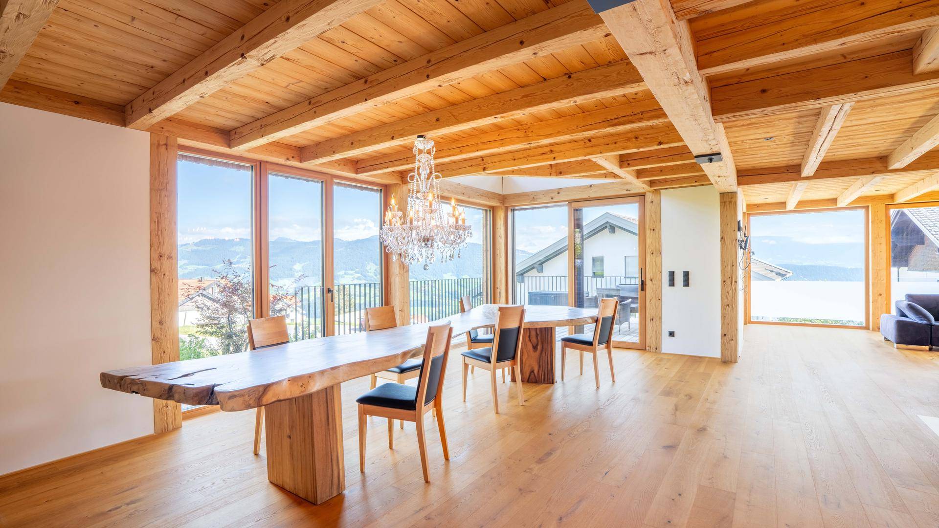 Heller Essbereich mit großem Holztisch, Kronleuchter und Panoramablick durch bodentiefe Fenster.