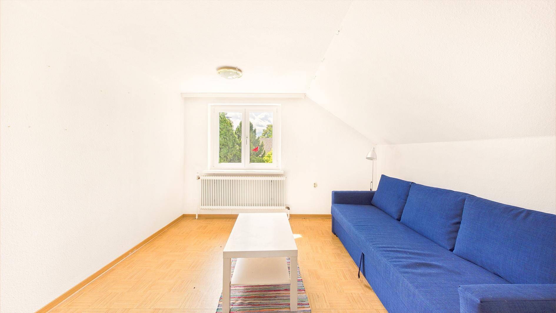 Gemütliches Wohnzimmer im Dachgeschoss mit blauer Couch und Holzboden, hell und einladend.