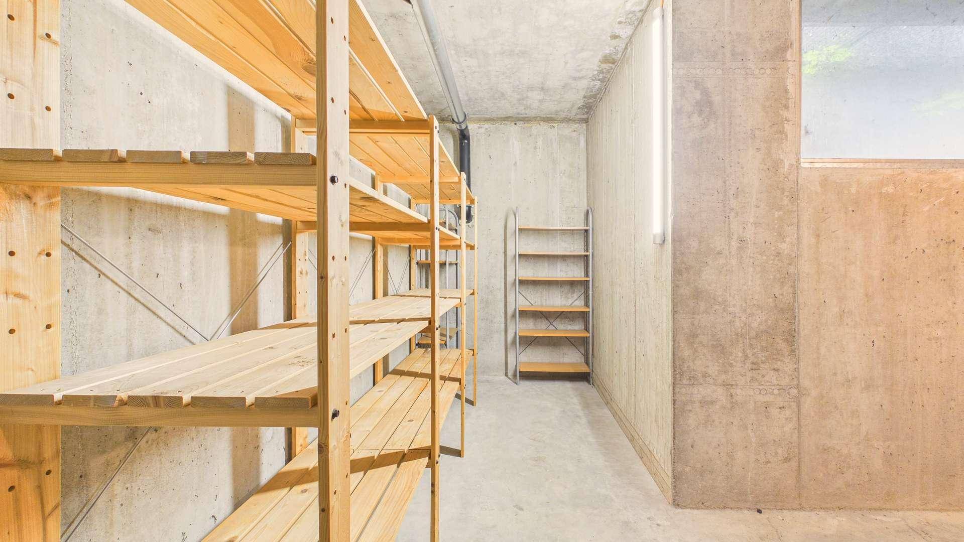 Geräumiger Kellerraum mit Betonwänden, Holzregalen und kleinem Fenster für natürliche Belüftung.