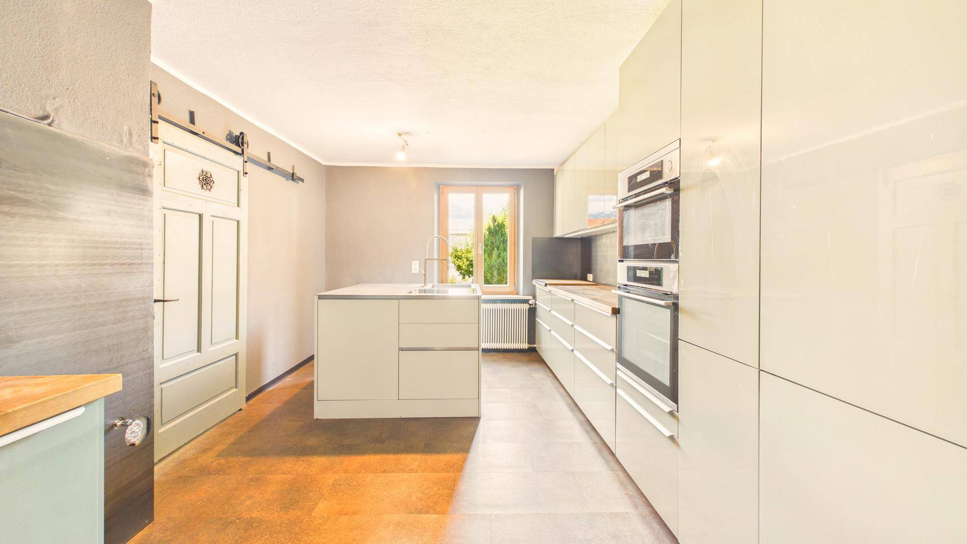 Helle moderne Küche mit Kochinsel, Fenster und Schiebetür im Landhausstil.