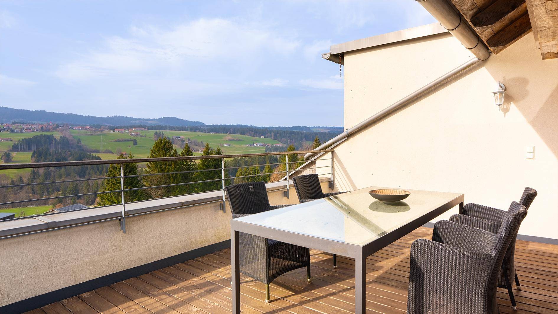 Geräumige Holzterrasse mit Esstisch und Stühlen, bietet einen weiten Blick über die Landschaft.