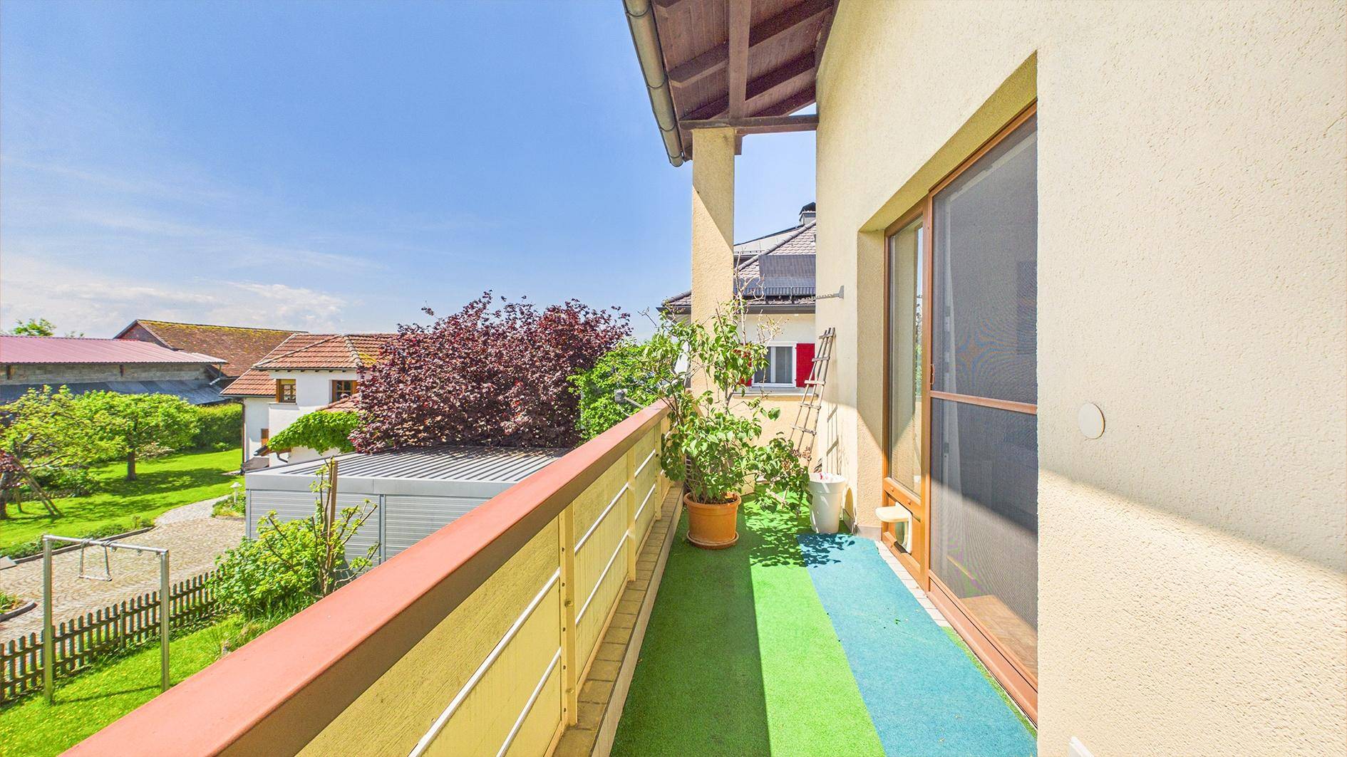 Sonniger Balkon mit Kunstrasen, Pflanzen und weitem Blick auf die grüne Umgebung.