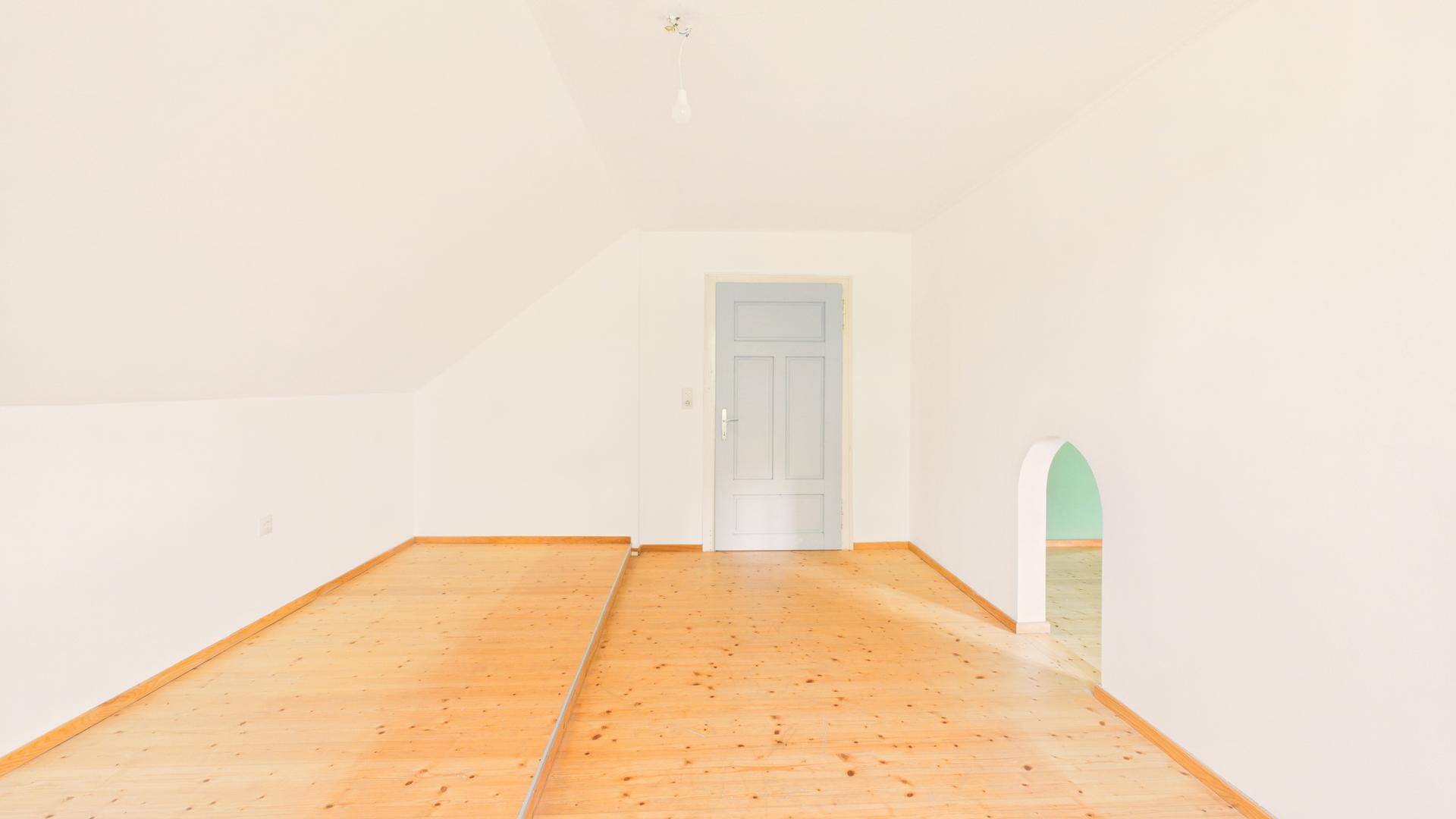 Helles Zimmer mit Holzboden, Dachschräge und einem Durchgang zu einem weiteren Raum.