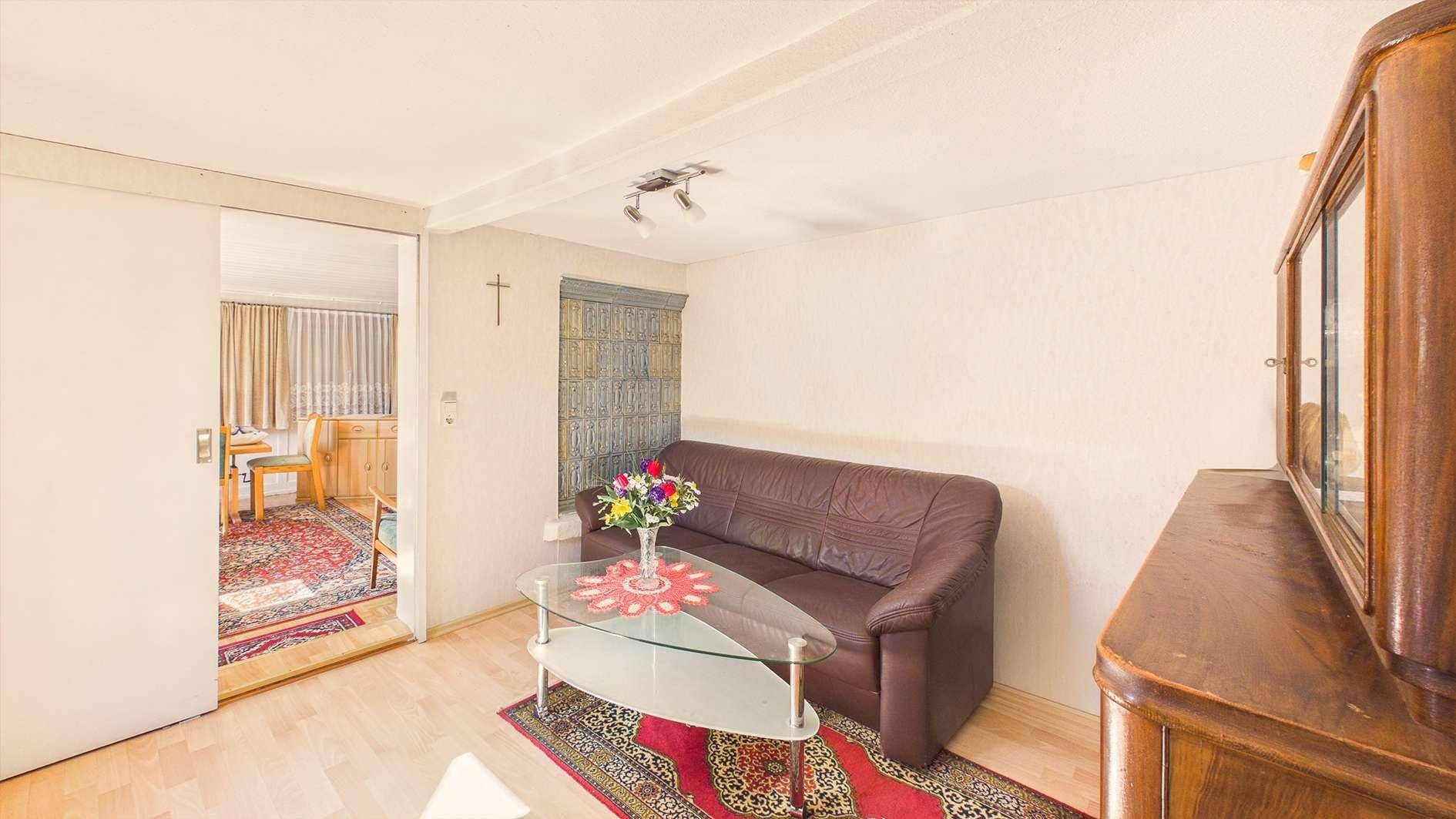 Wohnzimmer mit braunem Ledersofa, Holzboden und einem Durchgang zu einem weiteren Raum.