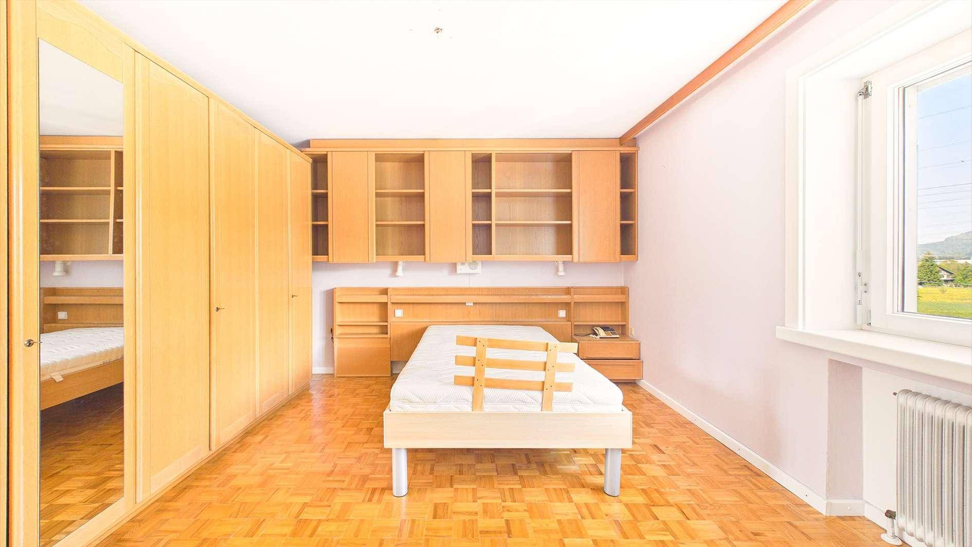 Schlafzimmer mit Holzboden, Bettgestell und integrierten Schränken und Regalen.