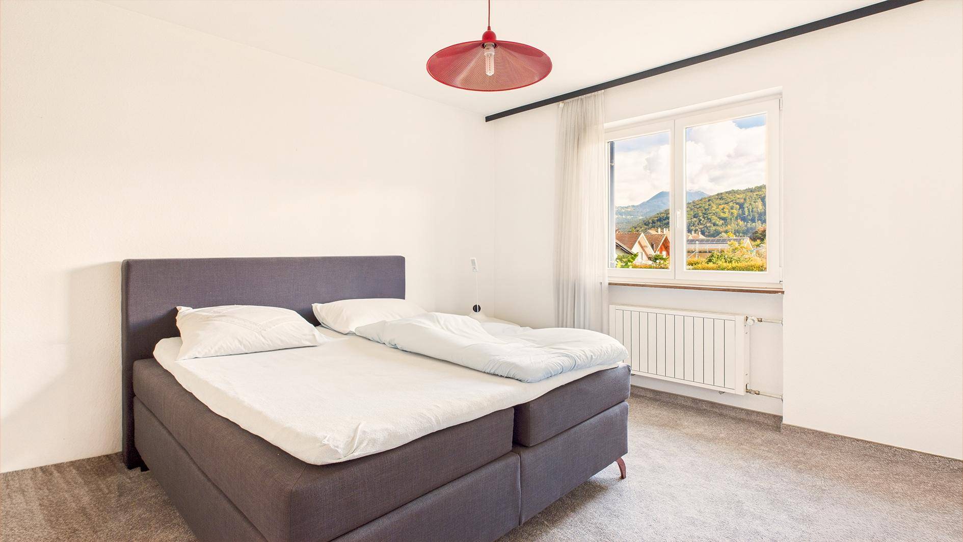 Helles Schlafzimmer mit Doppelbett, Teppichboden und Bergblick durch das Fenster.