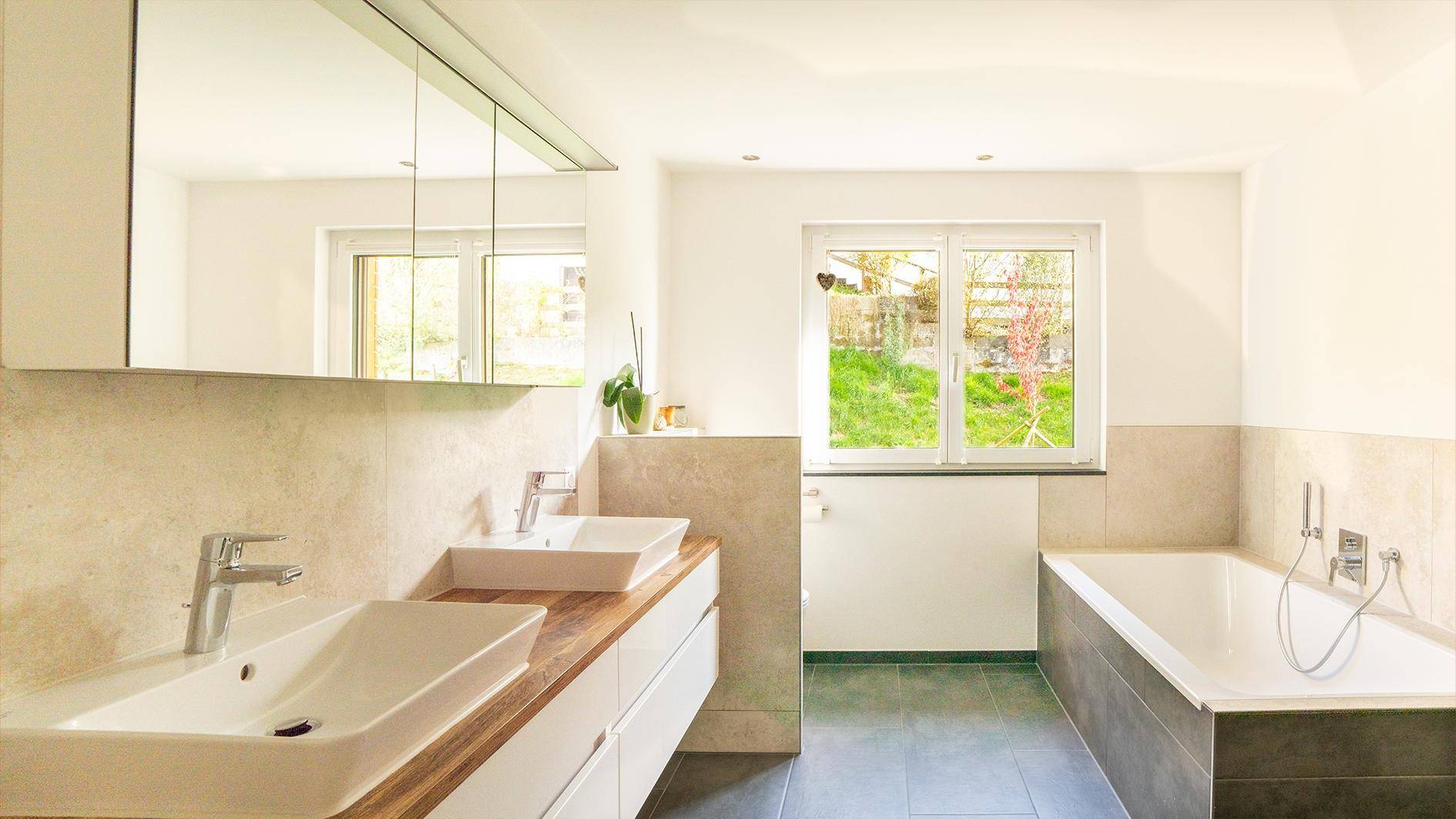 Modernes Badezimmer mit Doppelwaschbecken, Badewanne und Fenster mit Gartenblick.