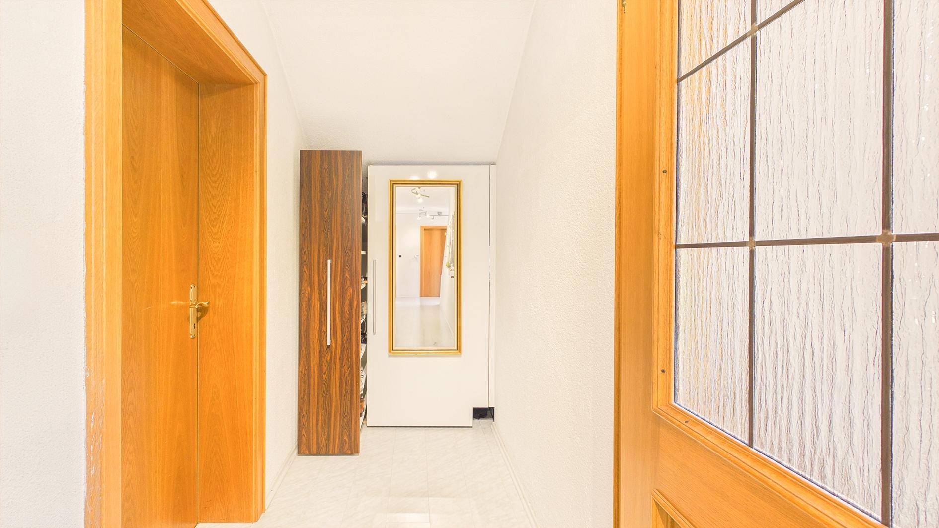 Heller Flur mit Holztüren, Garderobe und großem Spiegel.