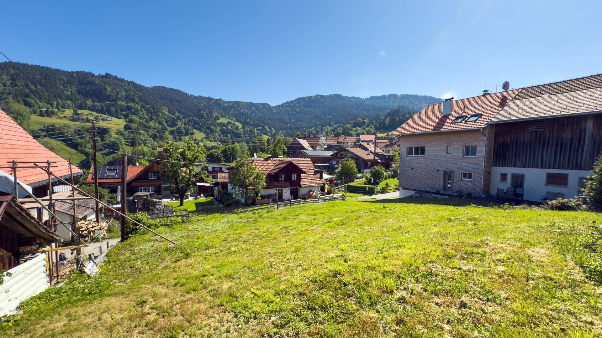 Weitläufiges grünes Grundstück mit Panoramablick auf die umliegende Berglandschaft und Häuser.