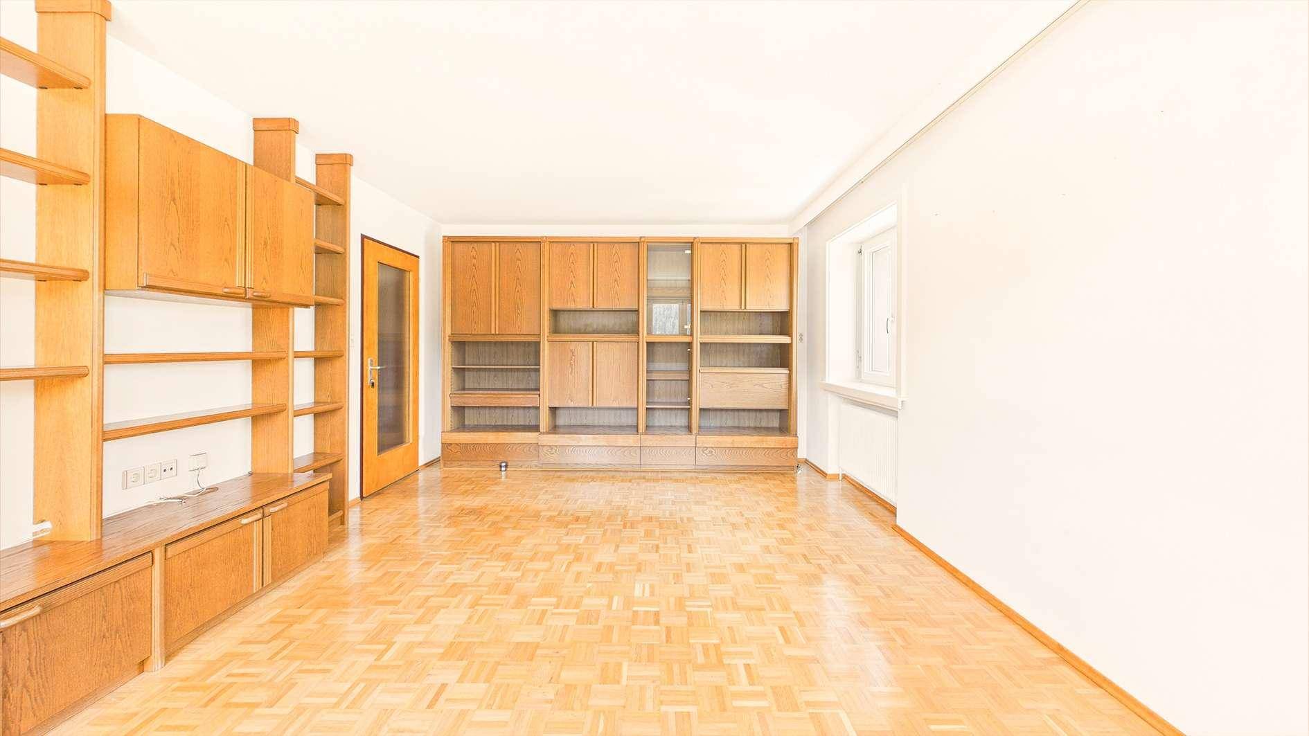 Heller Wohnbereich mit Parkettboden und umfangreichen Holz-Einbauschränken entlang der Wand.