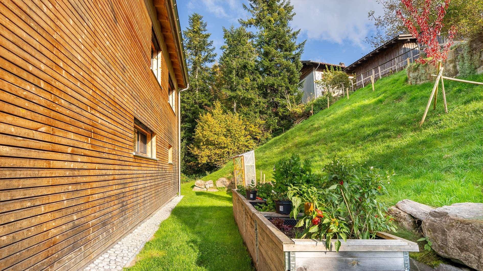 Seitenansicht des Hauses mit Holzfassade und einem kleinen Hochbeet für Kräuter und Gemüse.