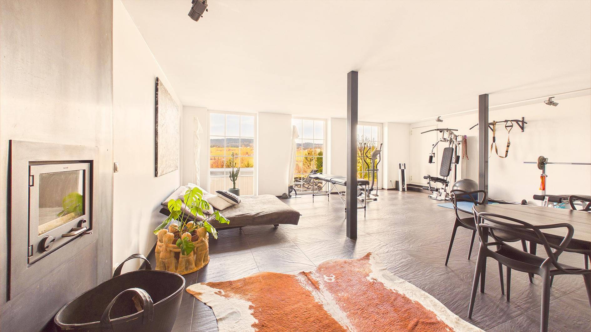 Offener Wohn- und Essbereich mit Kamin, Fitnessgeräten und großen Fenstern mit Aussicht.