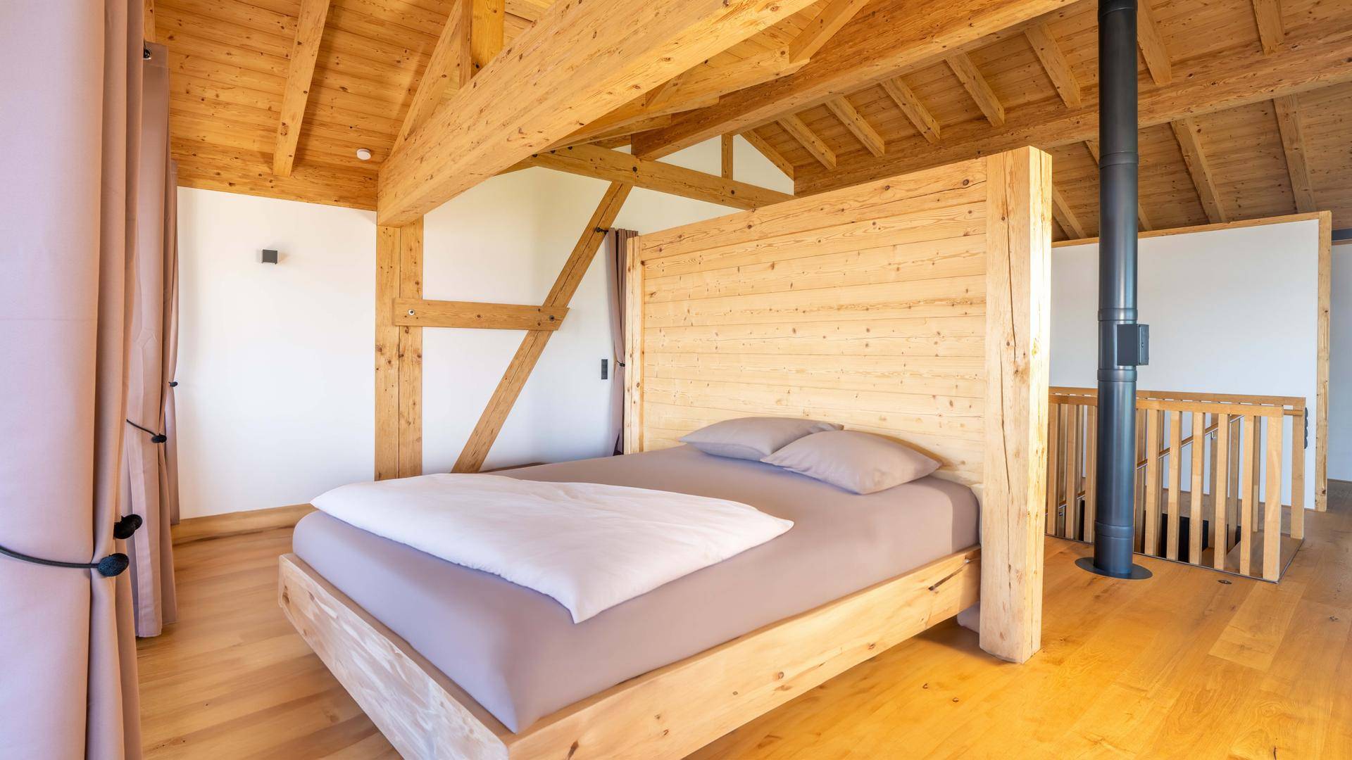 Geräumiges Schlafzimmer mit Holzbett, Holzbalkendecke und Blick auf die umliegende Landschaft.