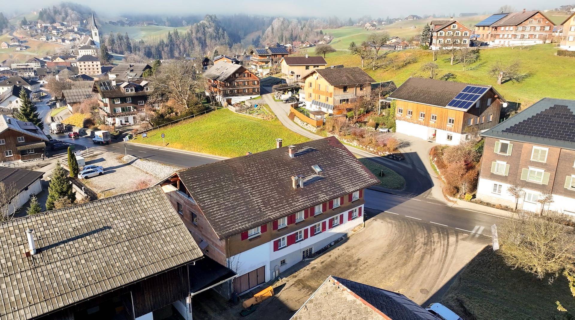 Luftaufnahme eines traditionellen Hauses mit rotem Dach und Fensterläden, umgeben von ländlicher Bebauung.