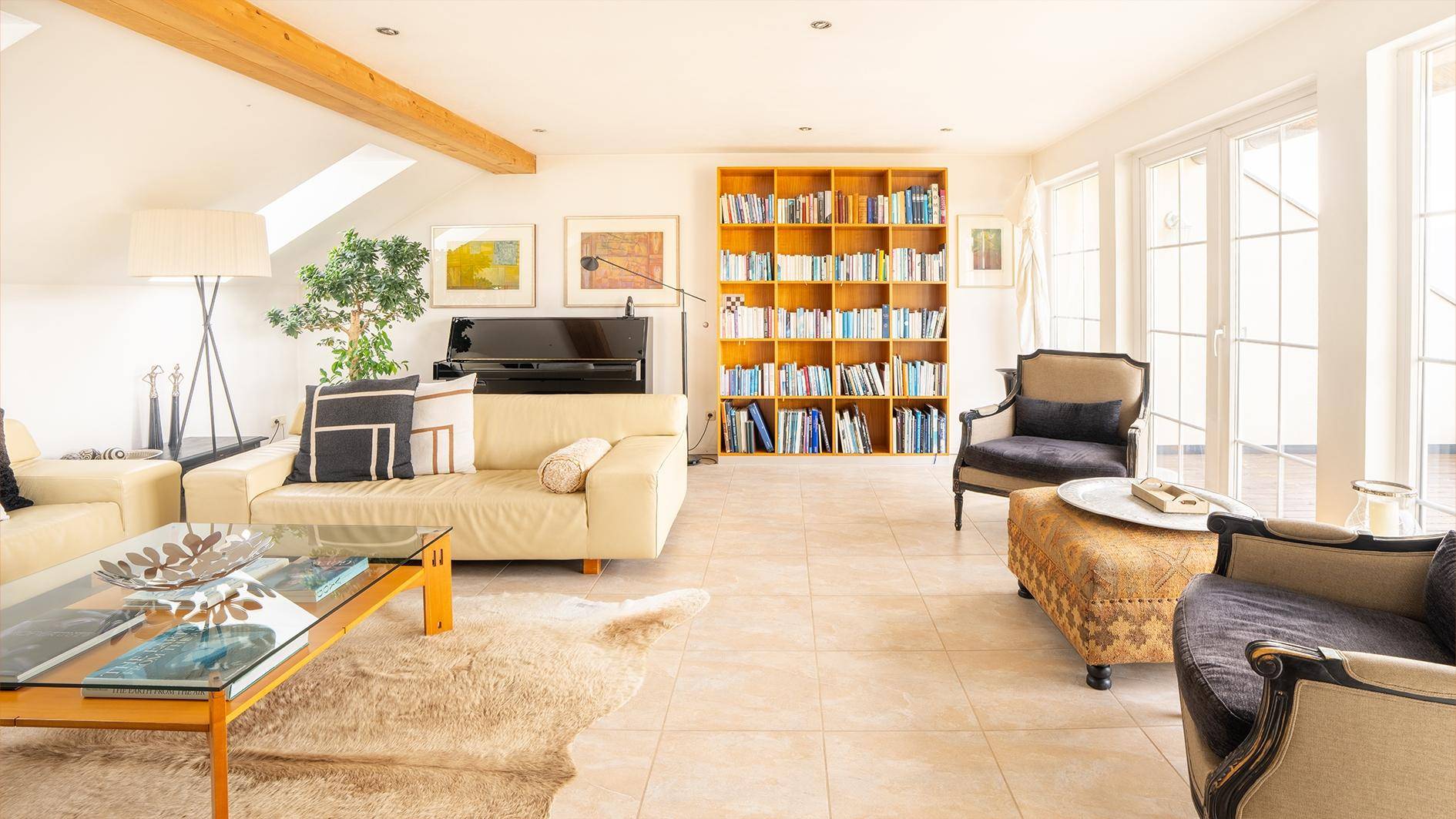 Lichtdurchflutetes Wohnzimmer mit beigen Sofas, Bücherregal und Zugang zur Terrasse.